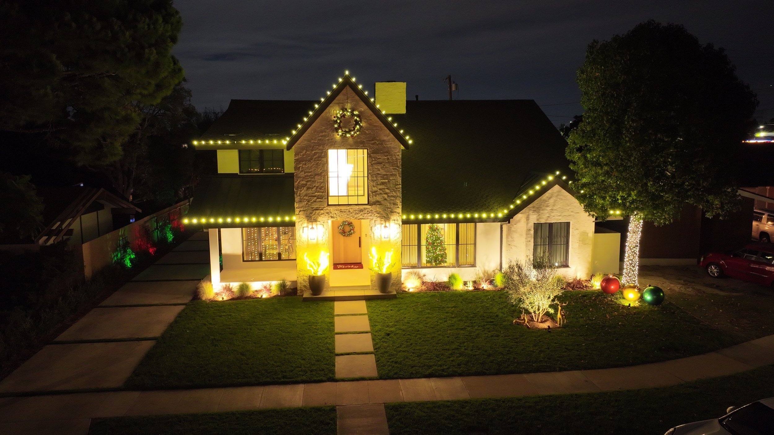 Professional holiday lighting installed on a two-story home in Long Beach, CA. Custom roofline lights and tree wrapping service.