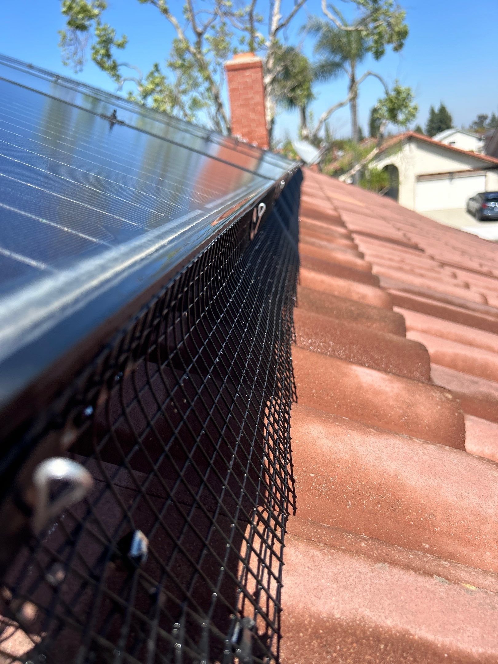 This close-up photo shows our bird proofing mesh securely installed along the perimeter of the solar panels on a tile roof in Cerritos, California. This mesh helps prevent pigeons and other birds from nesting underneath, protecting wiring and maintai