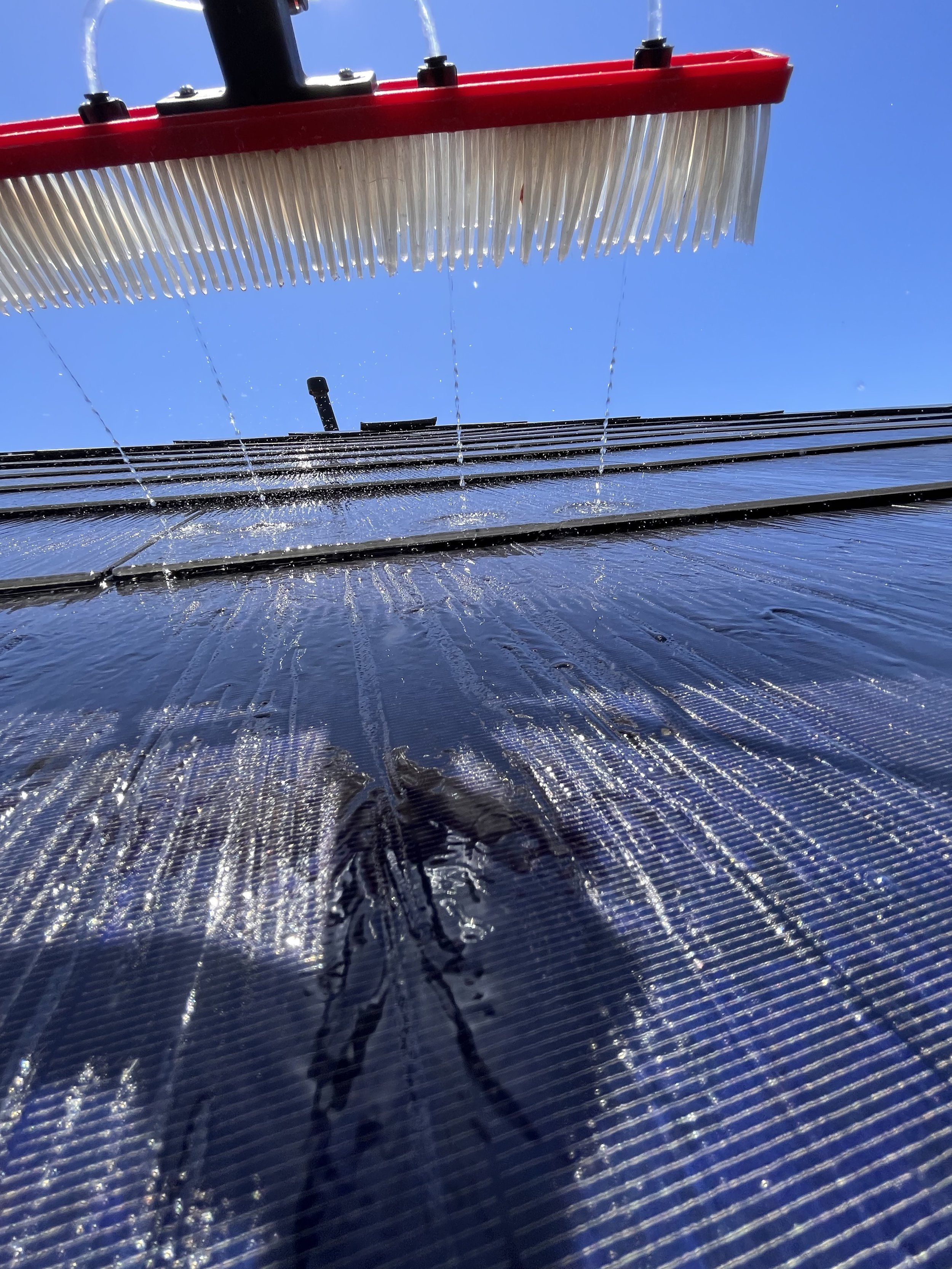Close-up view of a water-fed rotary brush being used to clean a Tesla solar roof on a sunny day in Long Beach, California. This soft, non-abrasive cleaning method removes dust, pollen, and salt buildup without damaging the surface, helping maintain s