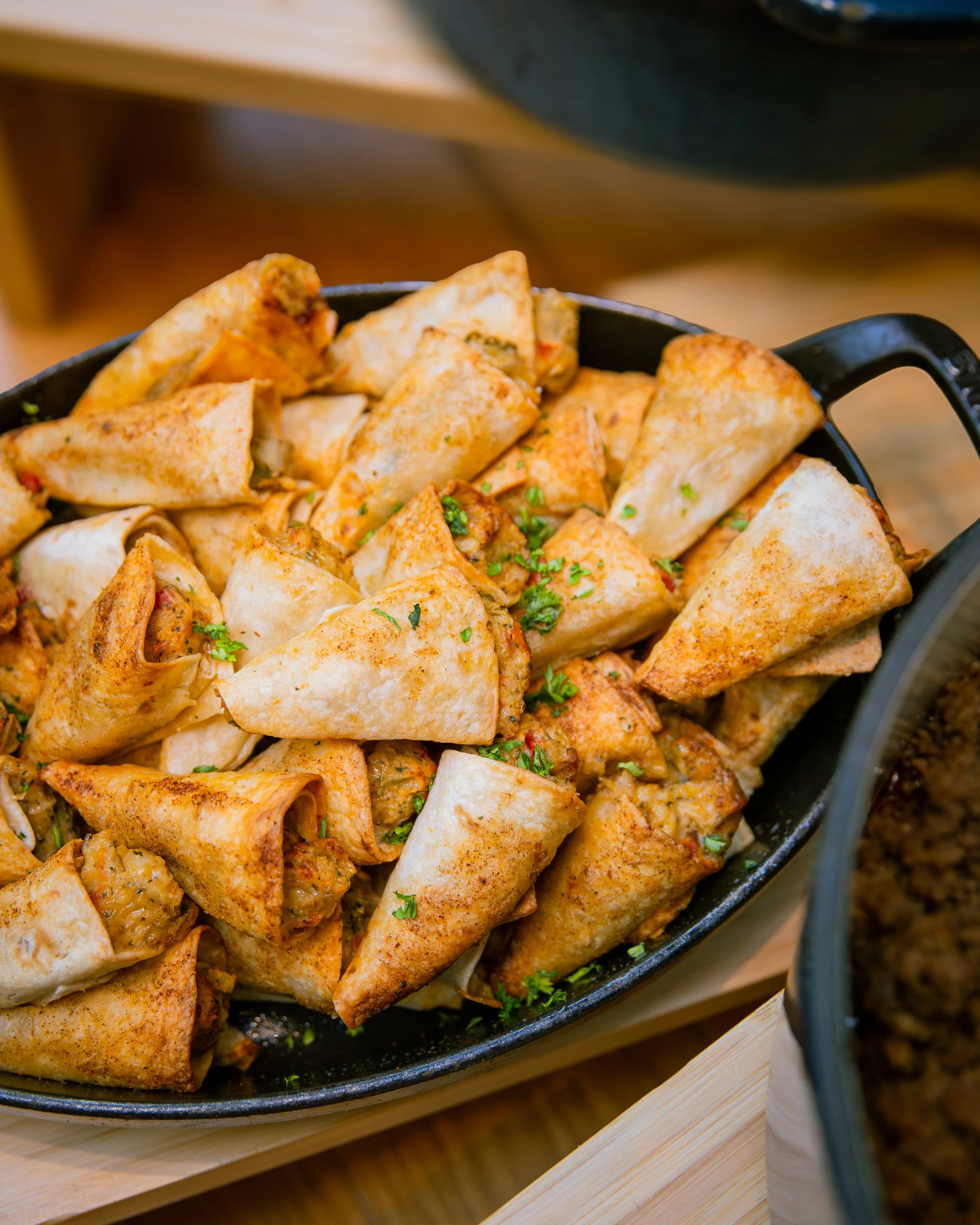 A black cast iron skillet filled with seasoned, cooked chicken and vegetable burritos garnished with chopped parsley.
