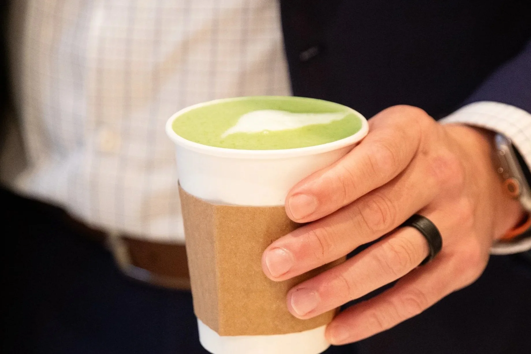Person holding a paper cup of green matcha latte with whipped cream.