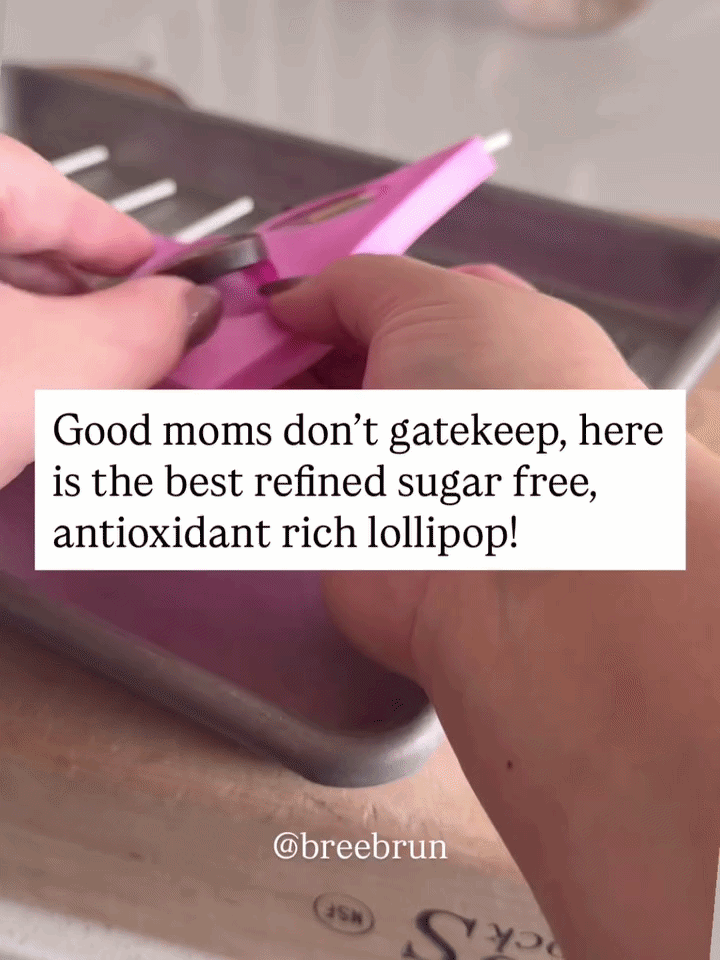 Hand lifting a dark brown homemade elderberry lollipop out of a pink silicone mold with text reading "Good moms don't gatekeep, here is the best refined sugar free".