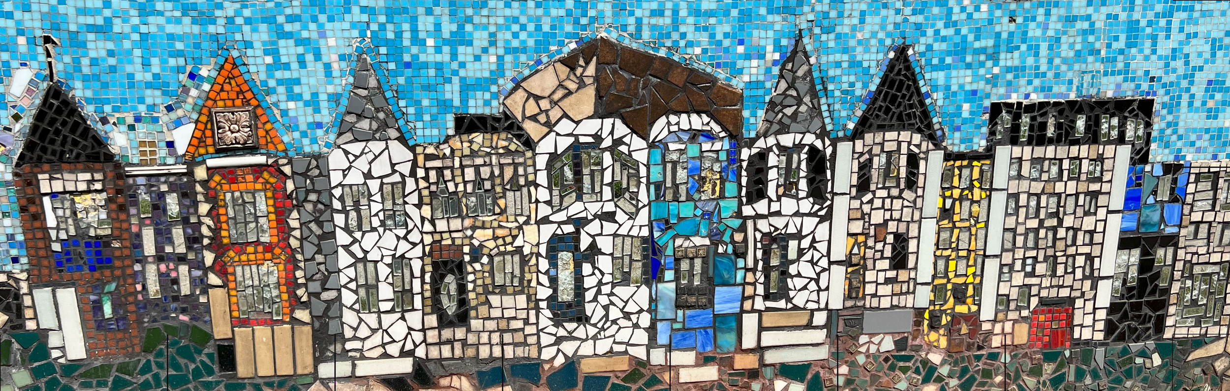 Colorful mosaic mural of a row of houses with varied architectural styles and bright colors, under a blue sky.