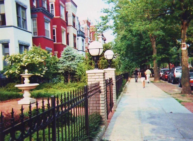 Street view with colorful apartment buildings, a sidewalk, trees, and pedestrians