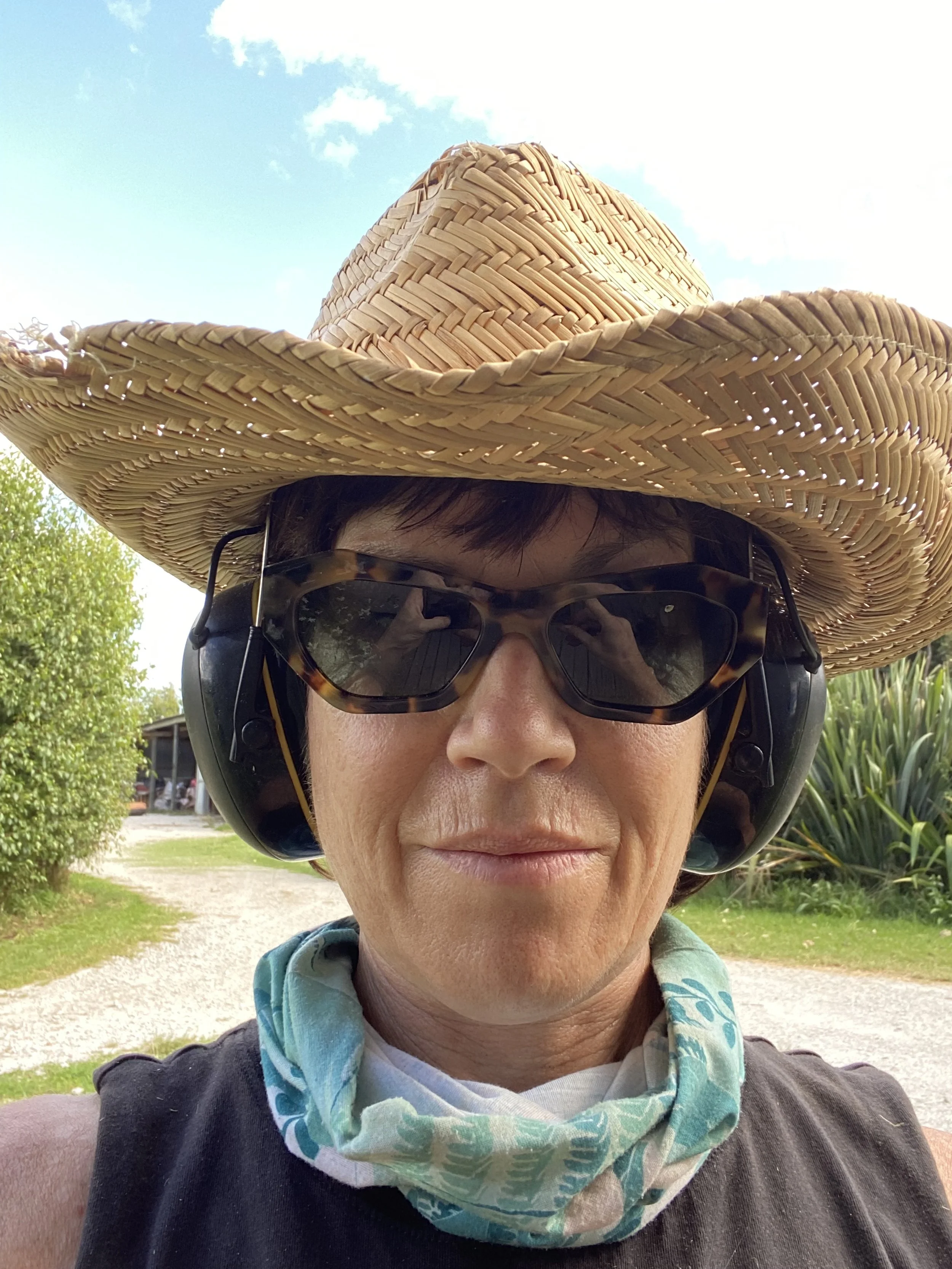 A person outdoors wearing a wide-brimmed straw hat, sunglasses, and a neck gaiter.