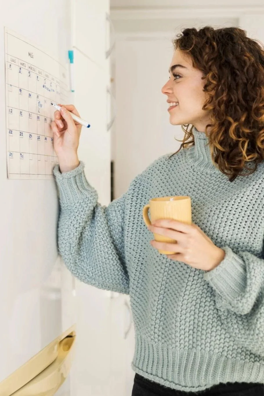 Young woman using a wall calendar to plan her week at home.