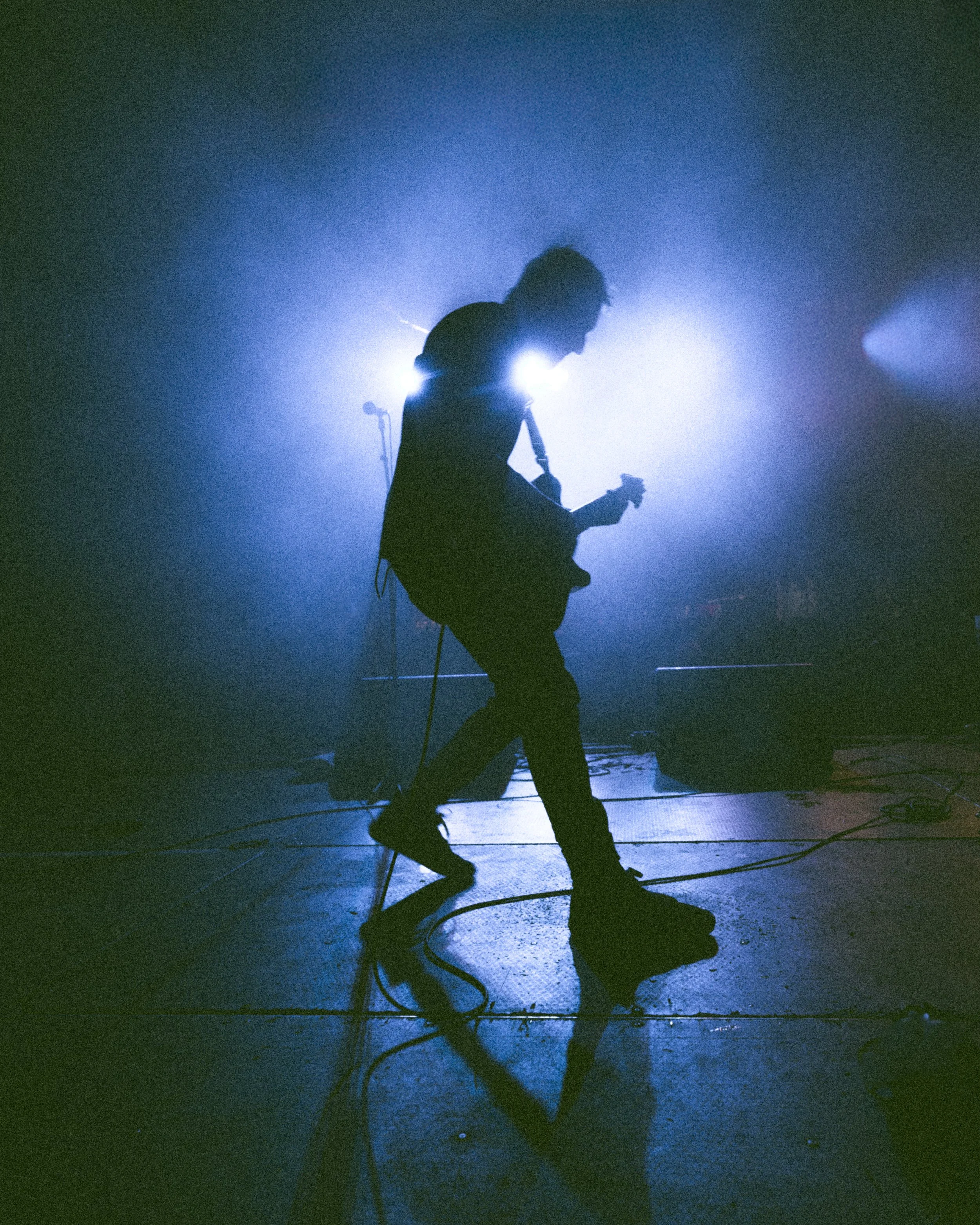 A silhouette of a guitarist performing on stage with bright backlighting creating a halo effect.