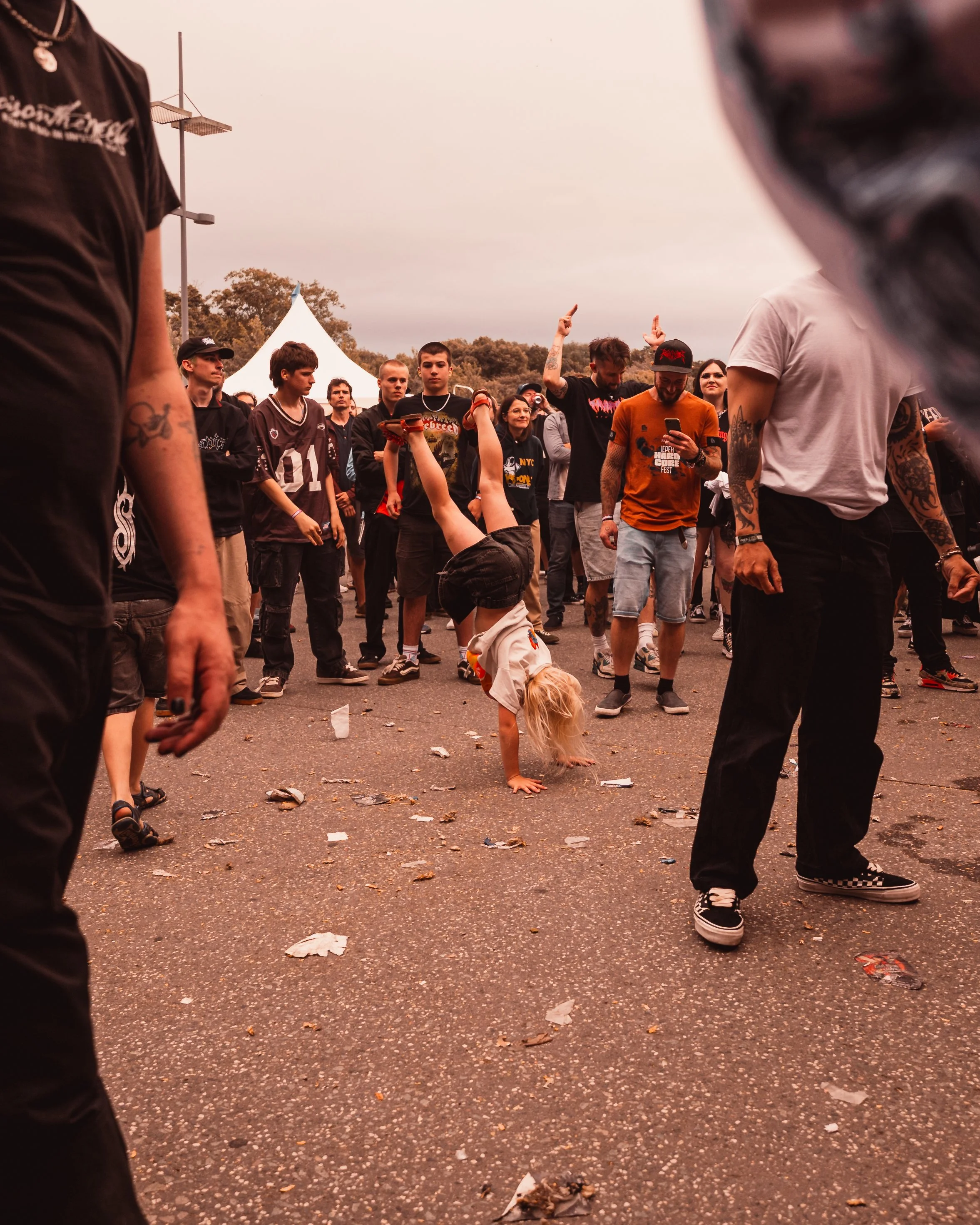 A young girl performing a handstand and breakdance move at an outdoor music festival with a crowd watching.