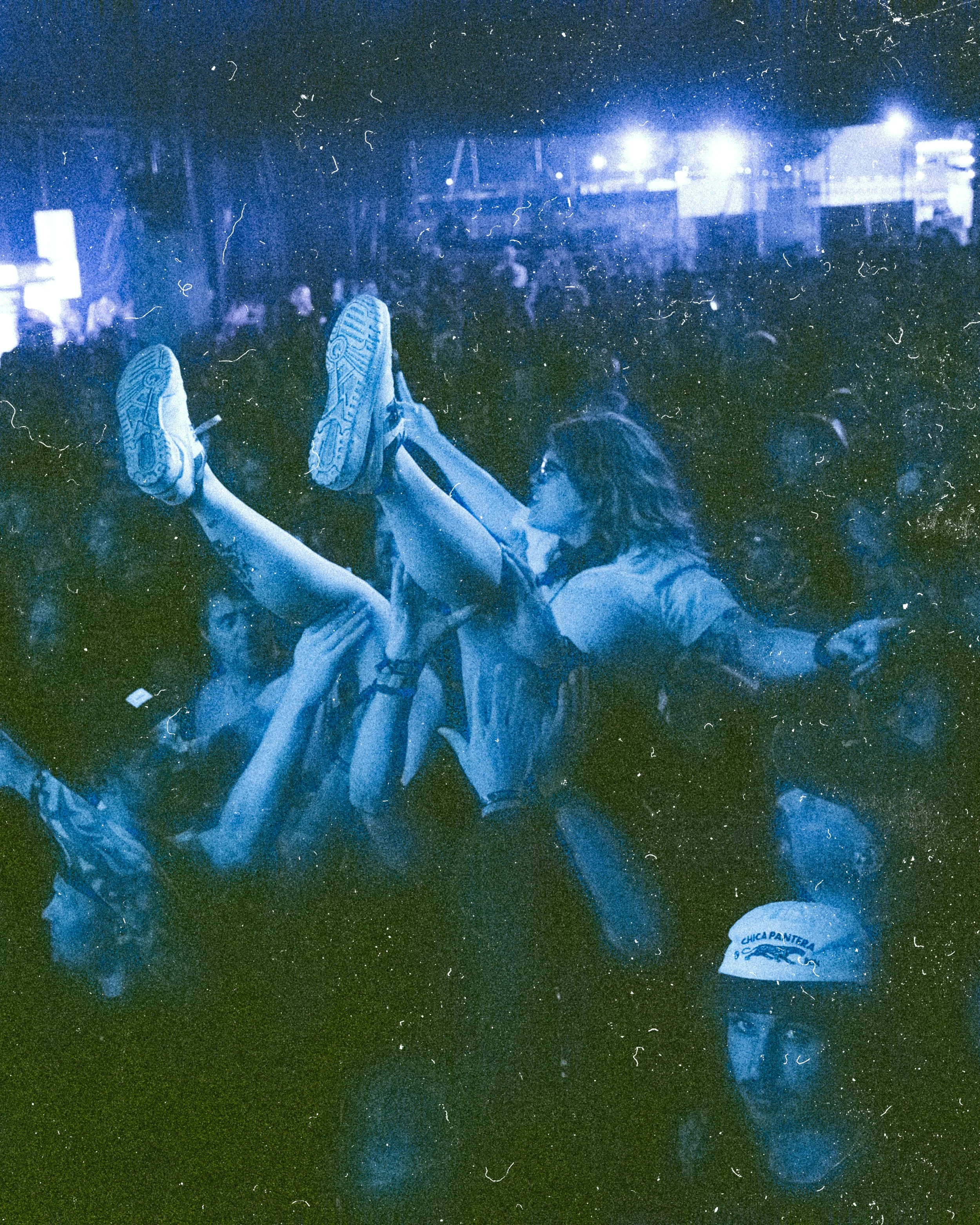 A woman being crowd surfed at a concert or festival at night, with people holding her up and a crowd in the background.