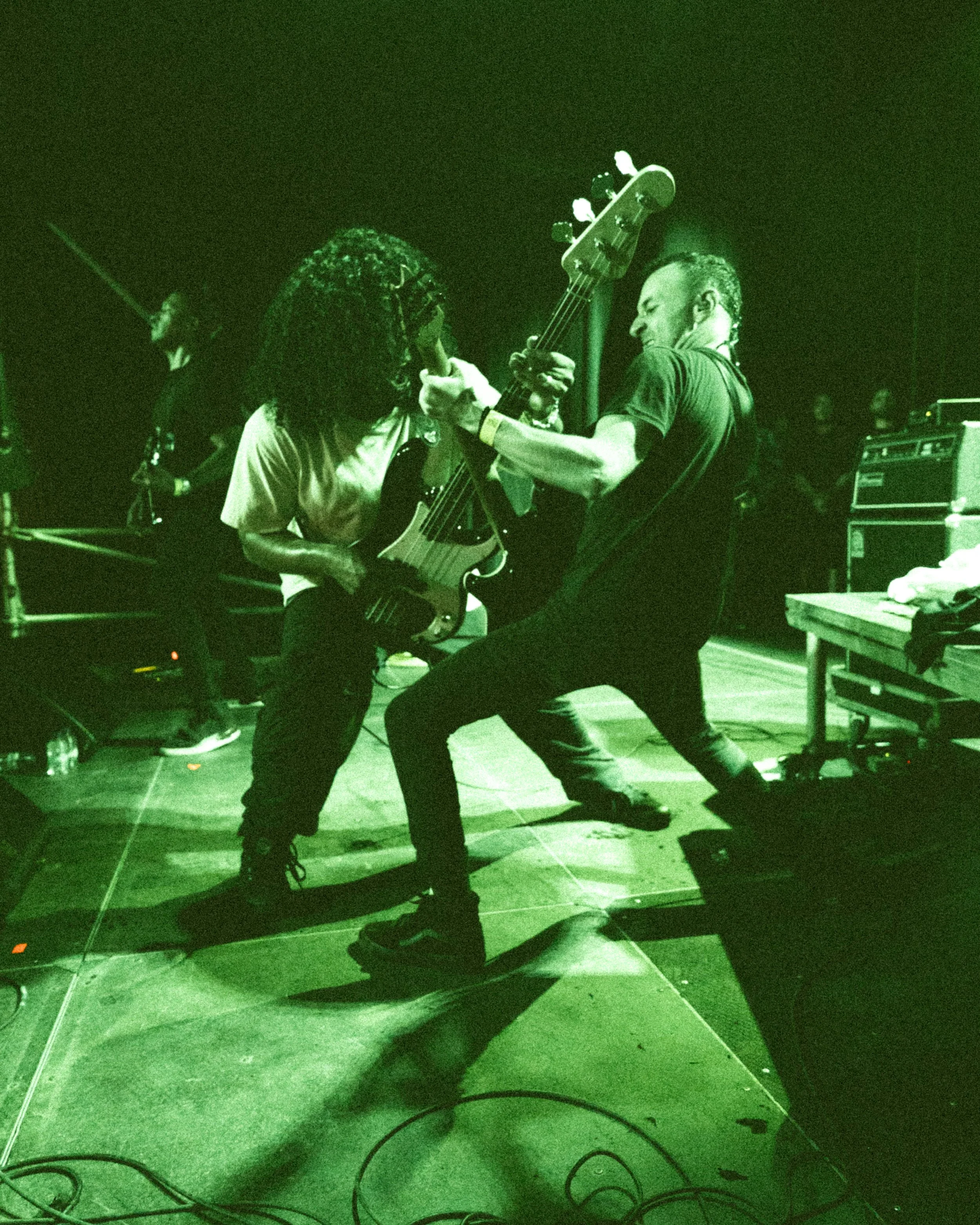 Musicians performing on stage, playing electric guitars in a green-tinted photo.