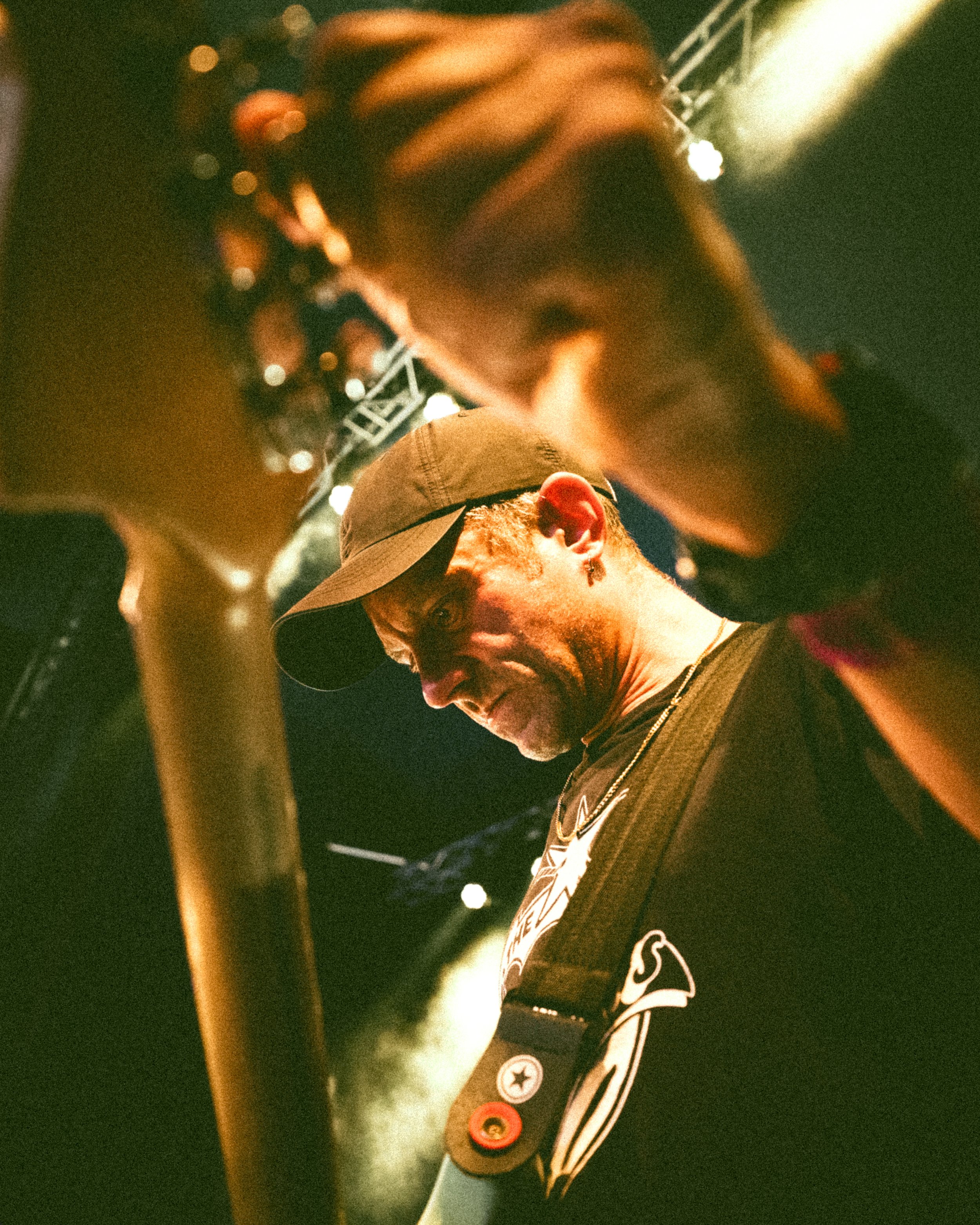 A musician on stage under concert lights, wearing a baseball cap and playing a guitar.
