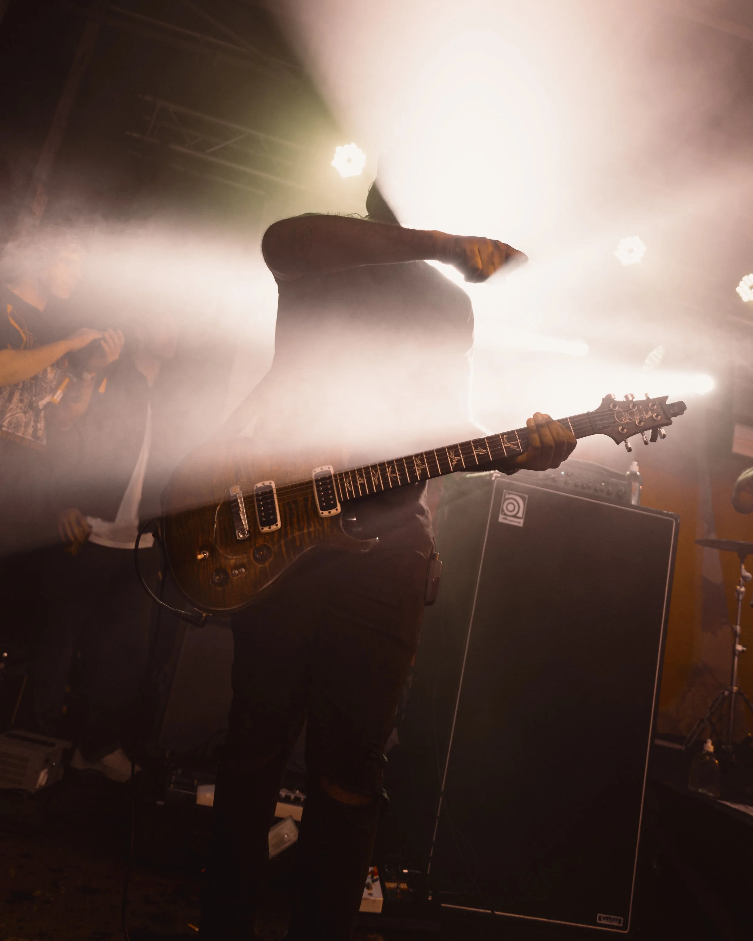A musician playing an electric guitar on stage with bright lights and fog.