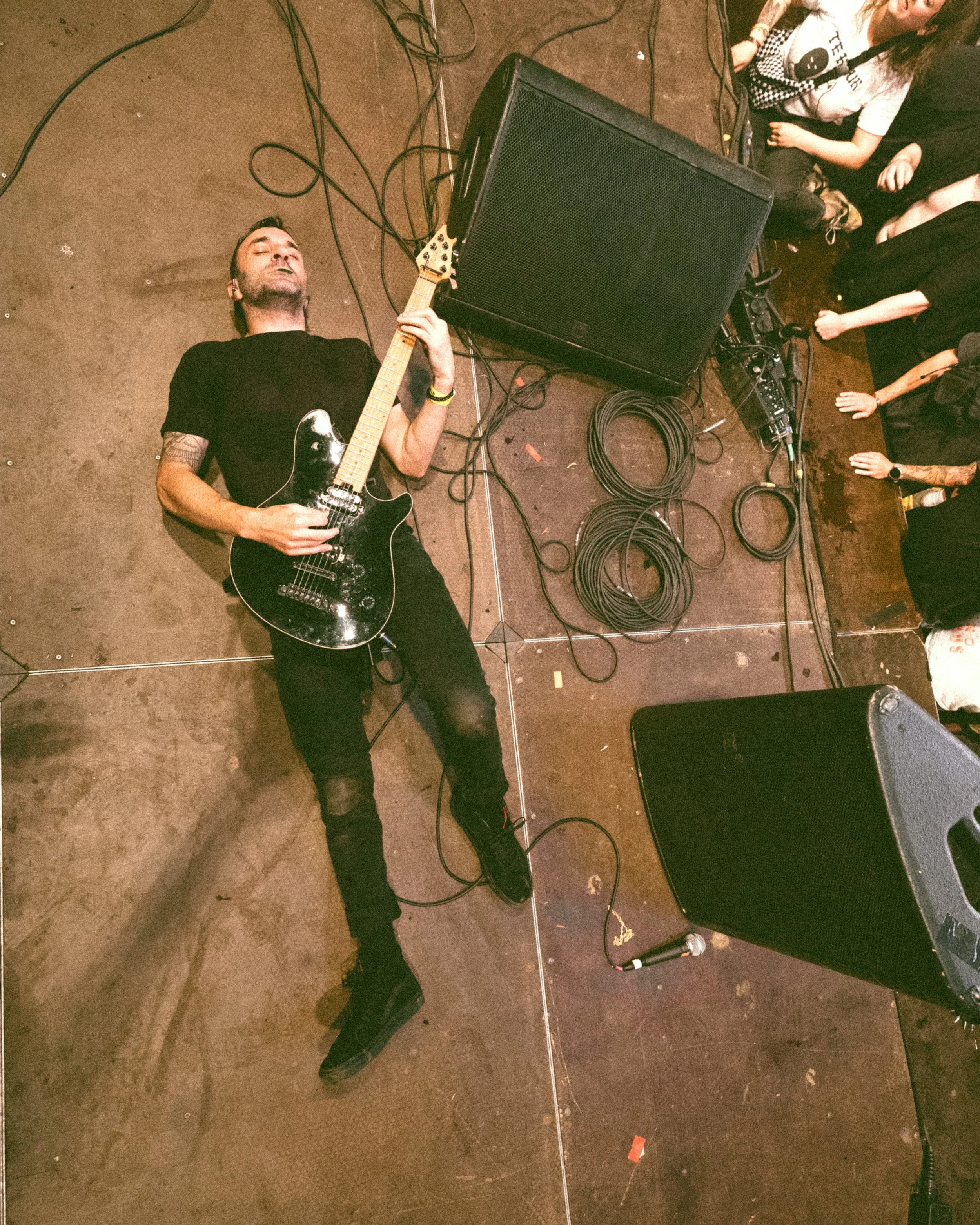 A musician lying on the stage playing an electric guitar during a live concert with a crowd watching.