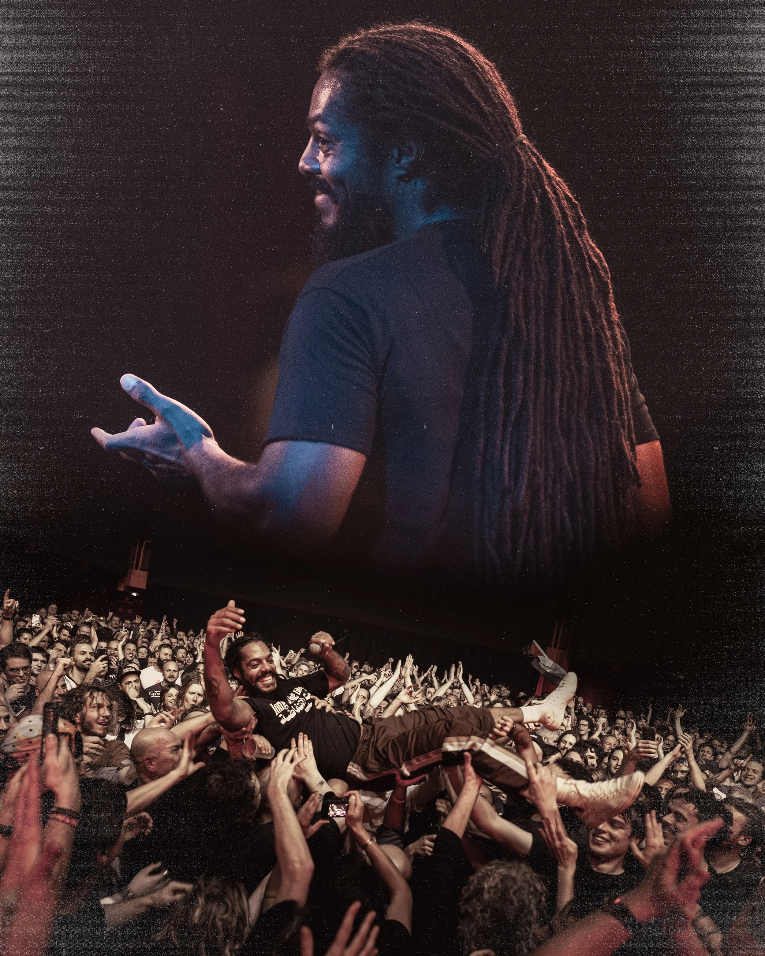 A man being crowd-surfed at a concert, with a large screen showing a smiling man with long dreadlocks in the background.