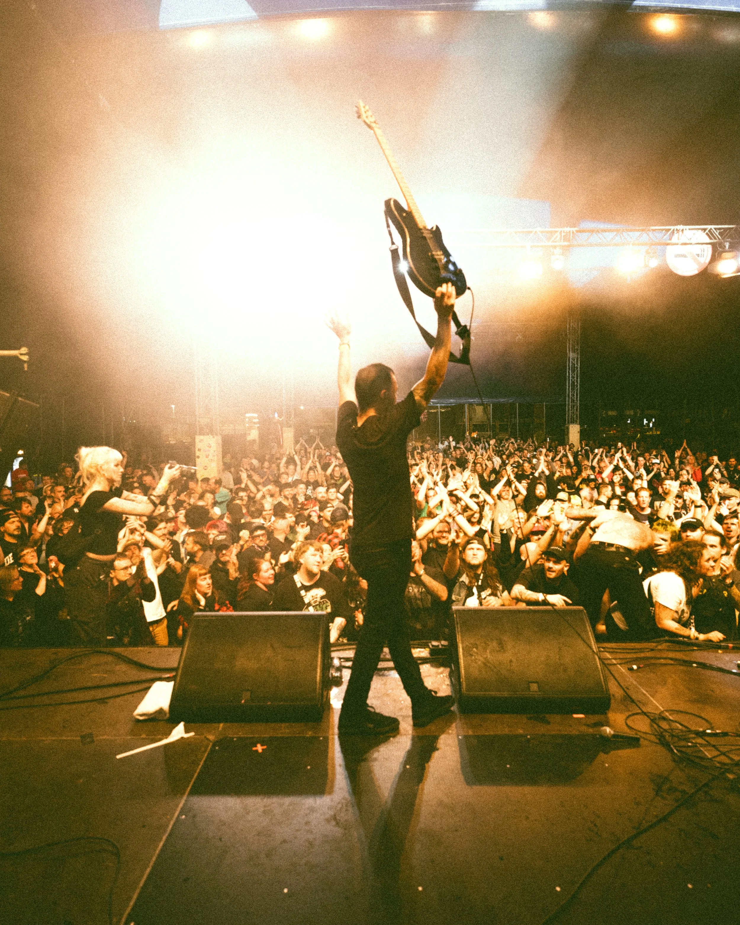 A musician on stage holding an electric guitar above his head towards a crowd at a concert.