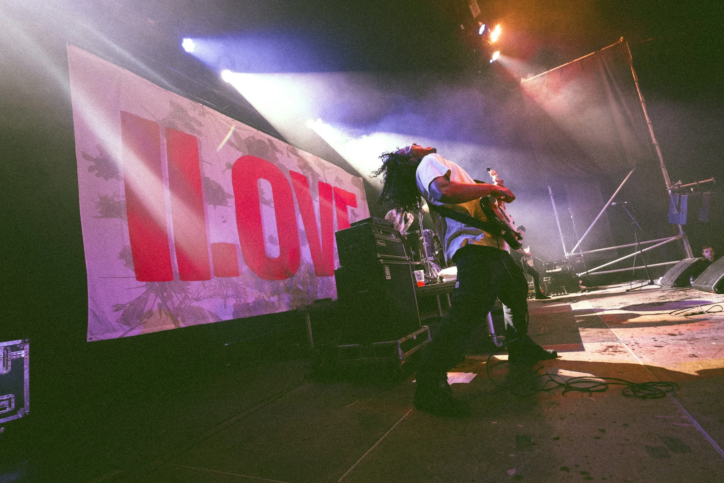 Musician playing electric guitar on stage during a live concert with a large LED screen displaying the word 'LOVE' in the background and stage lighting effects.