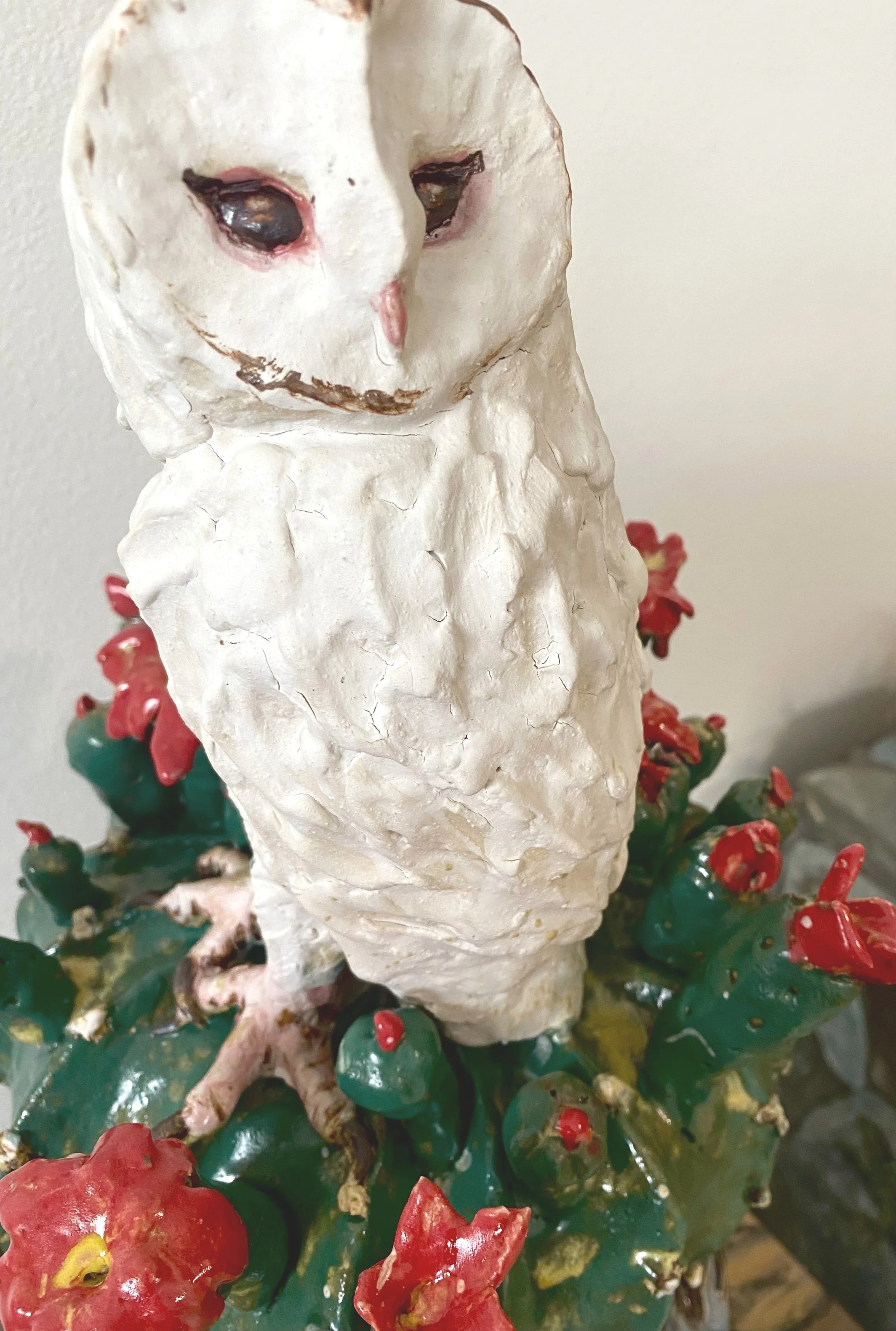 A ceramic figurine of an owl with a human-like face, sitting among red and green decorative elements.