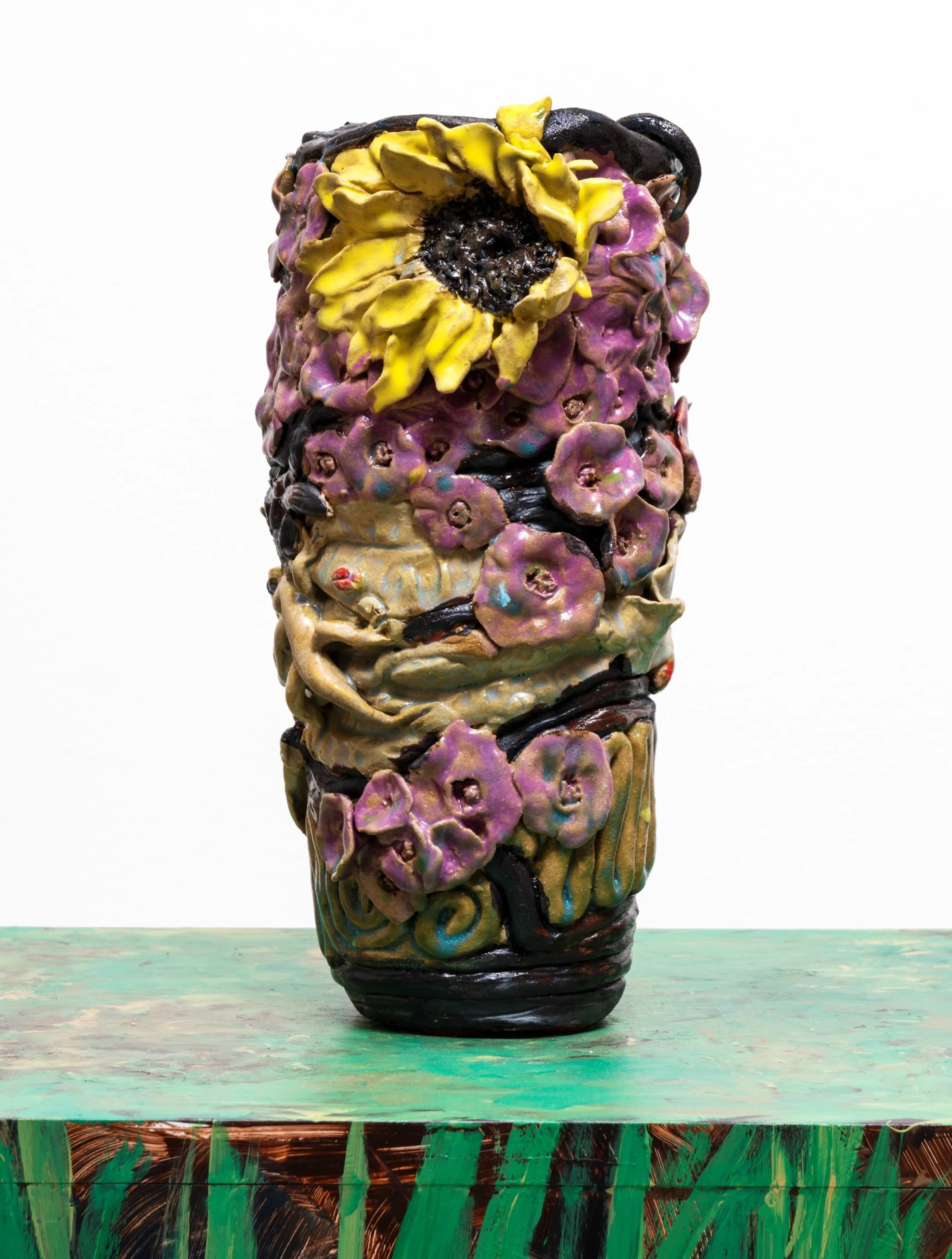 Colorful ceramic sculpture resembling a vase with abstract floral and organic patterns, placed on a green painted wooden surface.