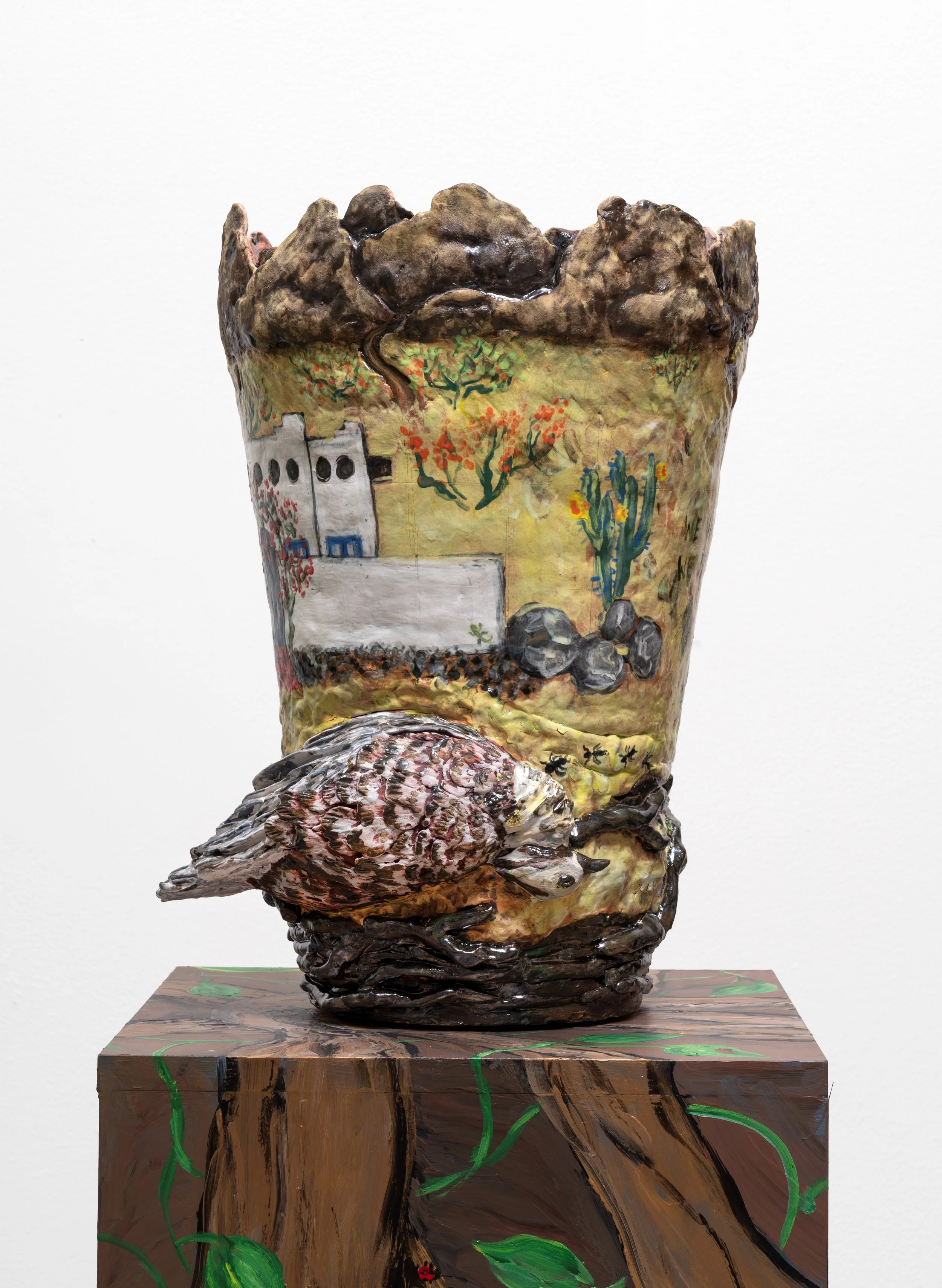 A ceramic sculpture featuring a landscape with trees, rocks, a white building, and a bird at the base, painted in a folk-art style.