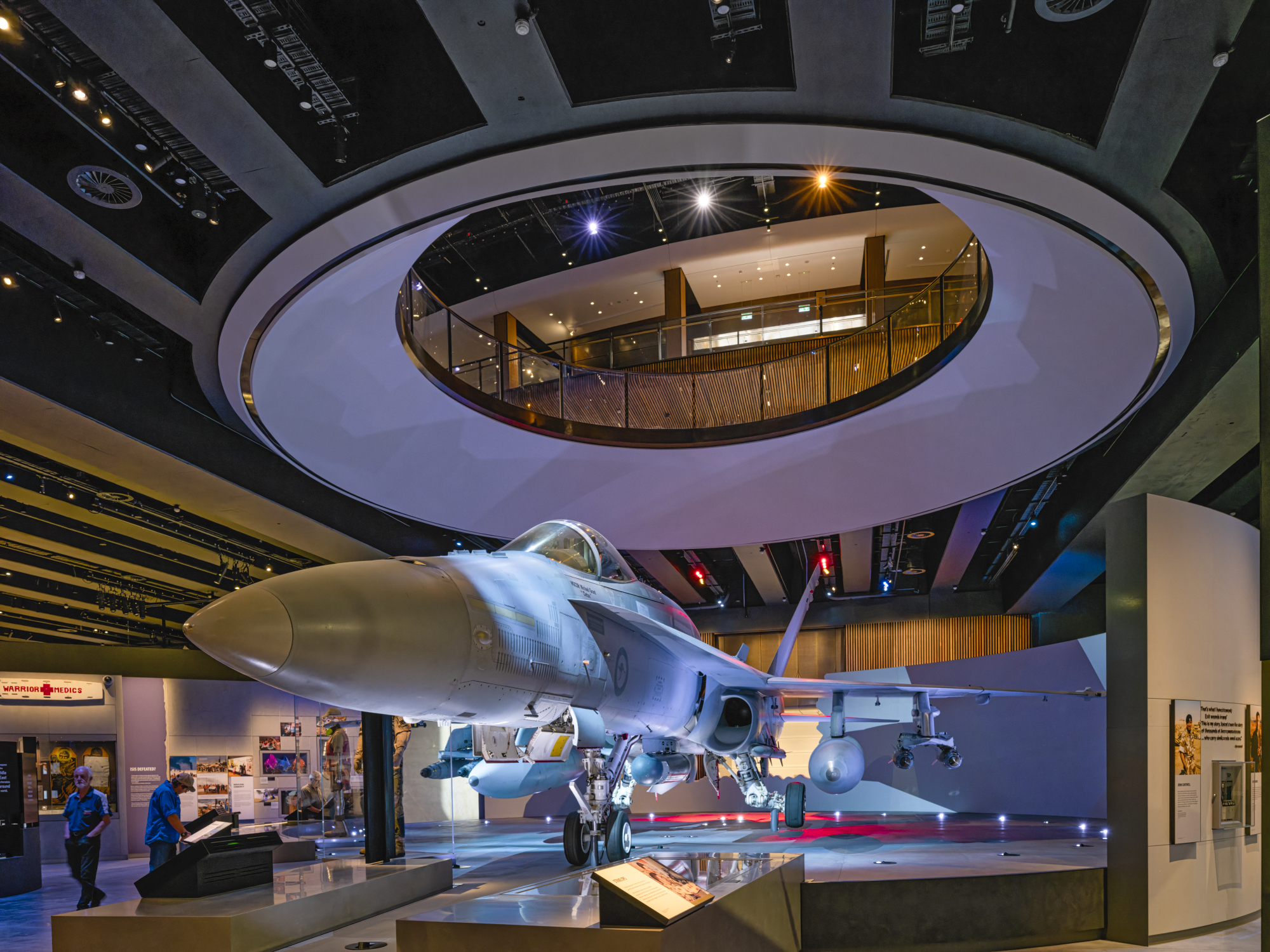 Inside a museum with a large fighter jet on display, colorful lighting, and a modern circular balcony visible overhead.