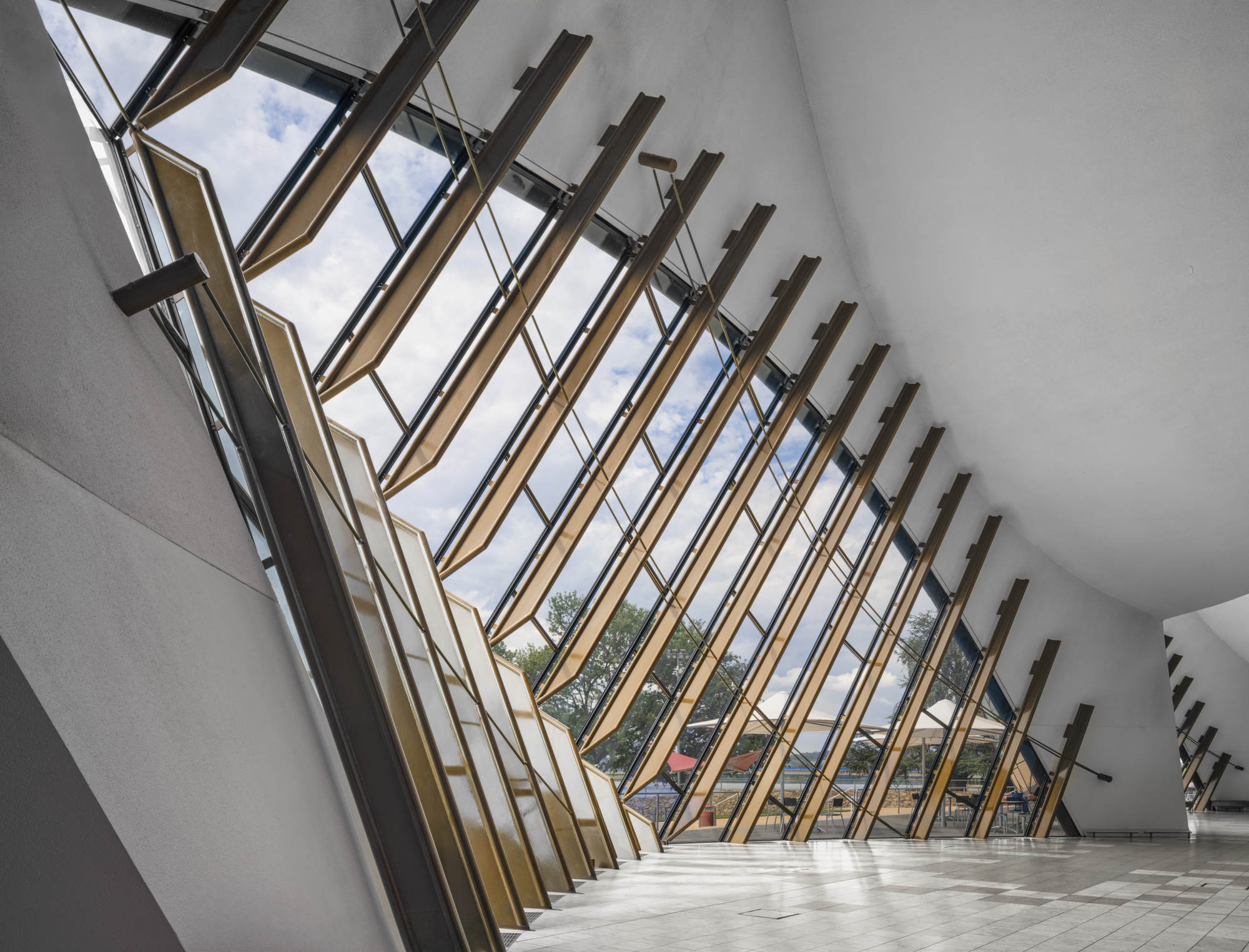 Interior view of a modern building with large glass windows and angled wooden beams.