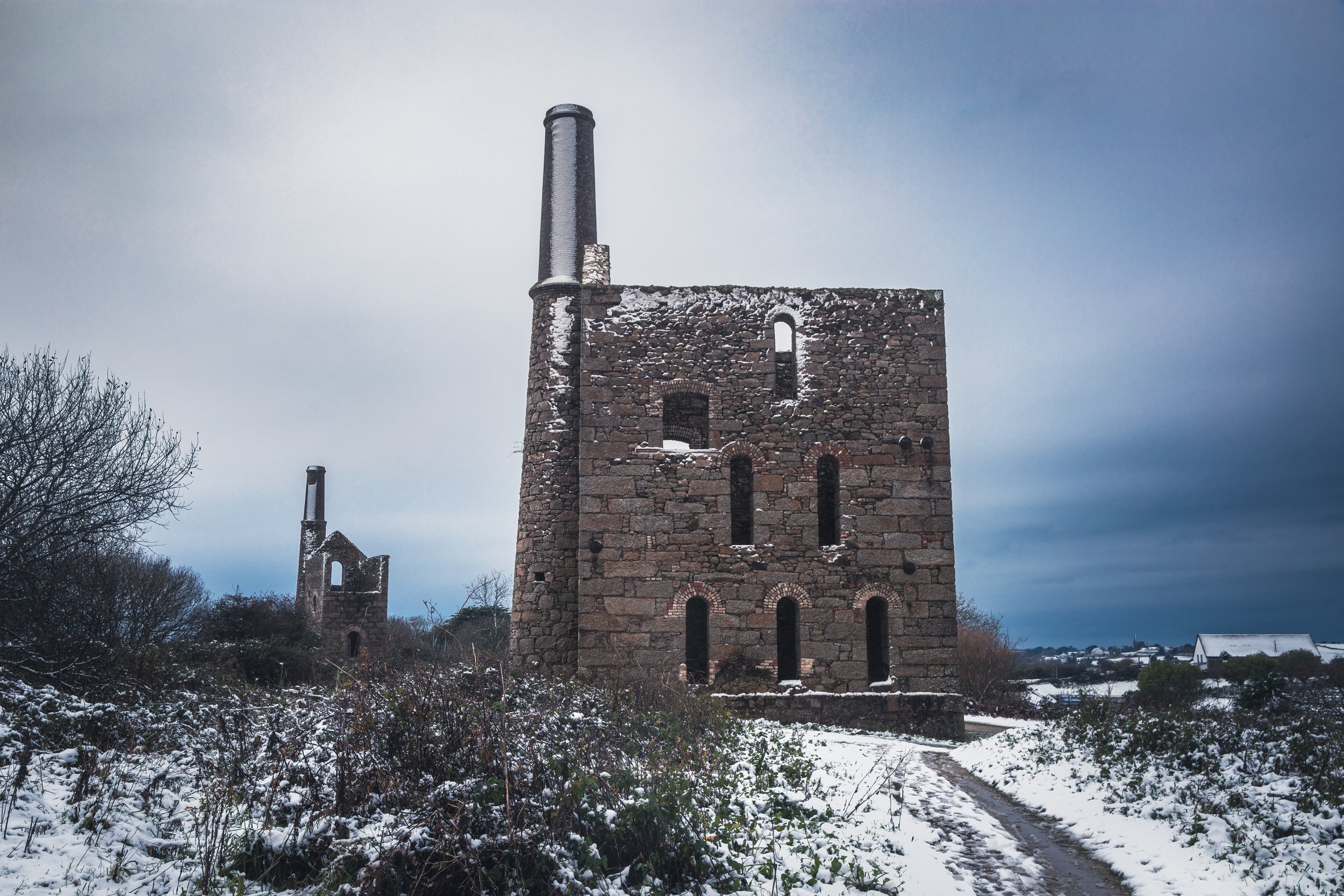 Snow-covered ruins of an old stone building with tall chimneys on a cloudy winter day.
