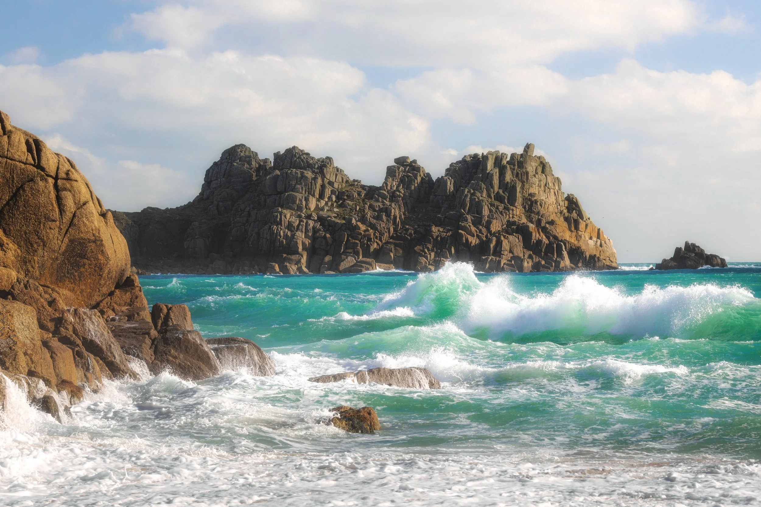Rocky coastline with waves crashing against rocks under a partly cloudy sky.