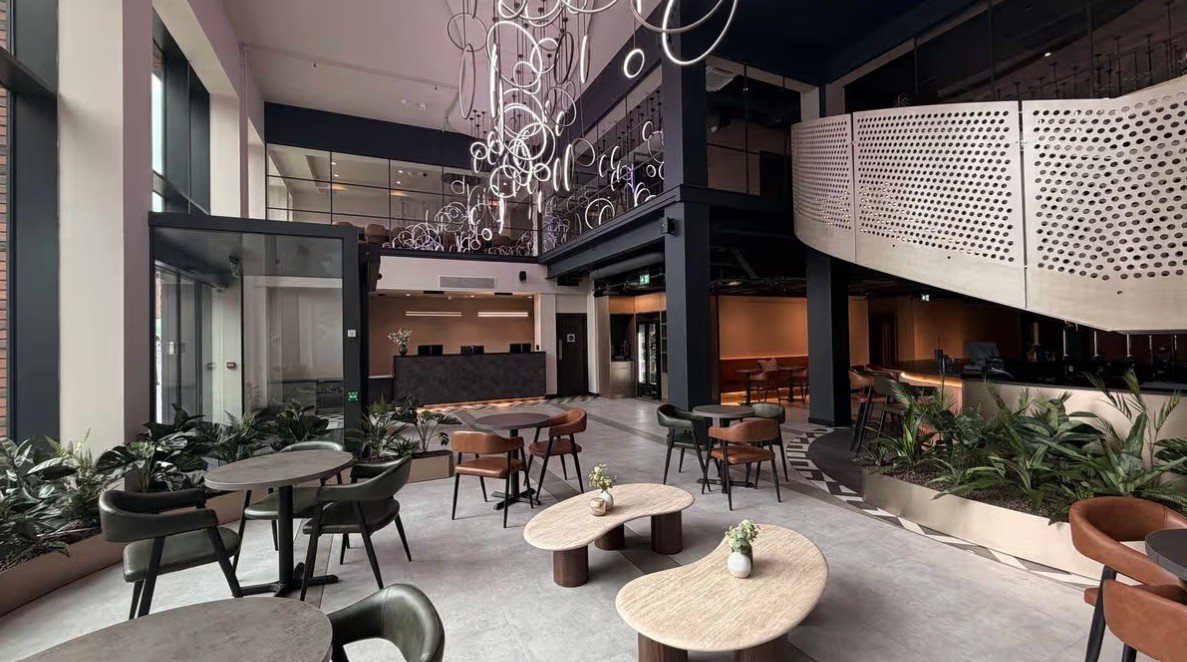 Hotel lobby interior at Aloft by Marriott Manchester City Centre, showcasing contemporary hospitality design with feature lighting, flexible lounge seating, natural materials, integrated planting and an open mezzanine space.