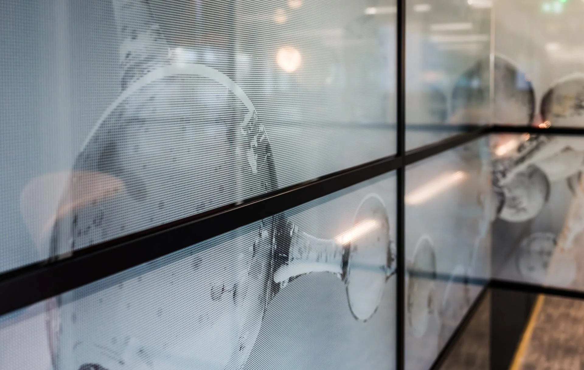 Close-up of a digital screen displaying a stylized black and white illustration of a person's face, with glasses and a beard, seen through a textured glass surface with reflections of inside lights.