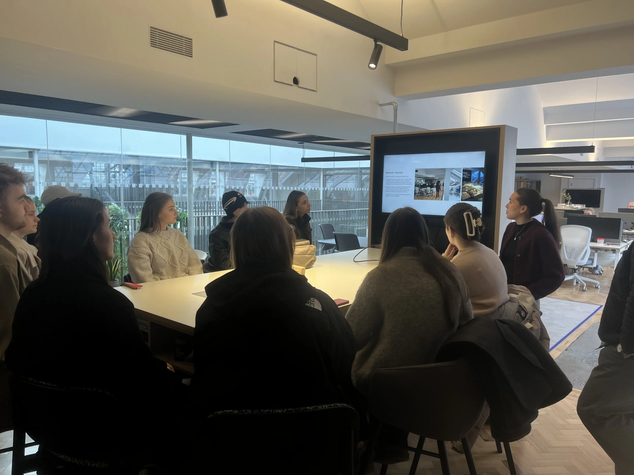 Manchester Metropolitan University design students in the SpaceInvader studio during Green Week, listening to a sustainability and interior design presentation in a modern workplace meeting space.