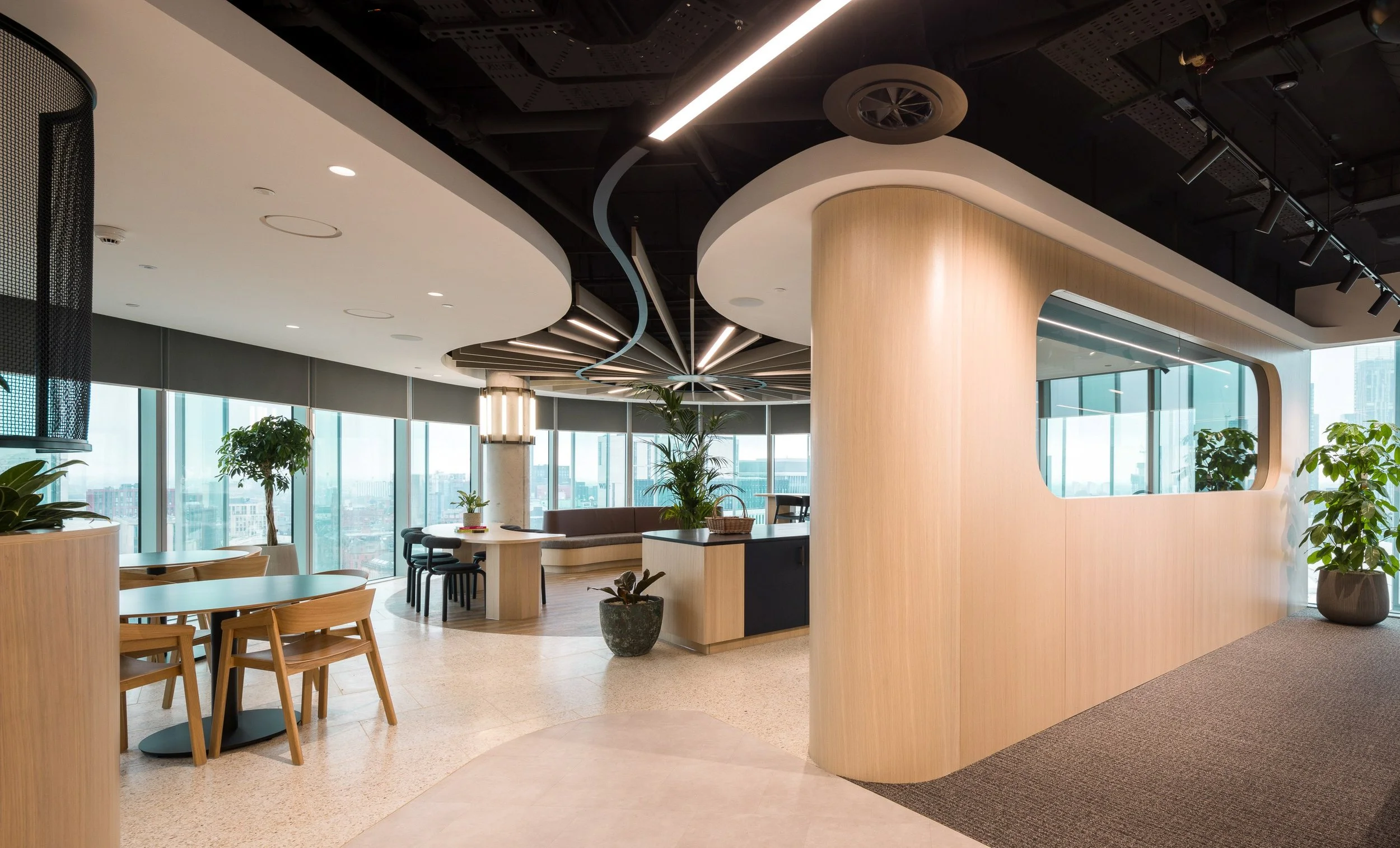 Modern office space with wooden accents, large windows, plants, and contemporary lighting fixtures.