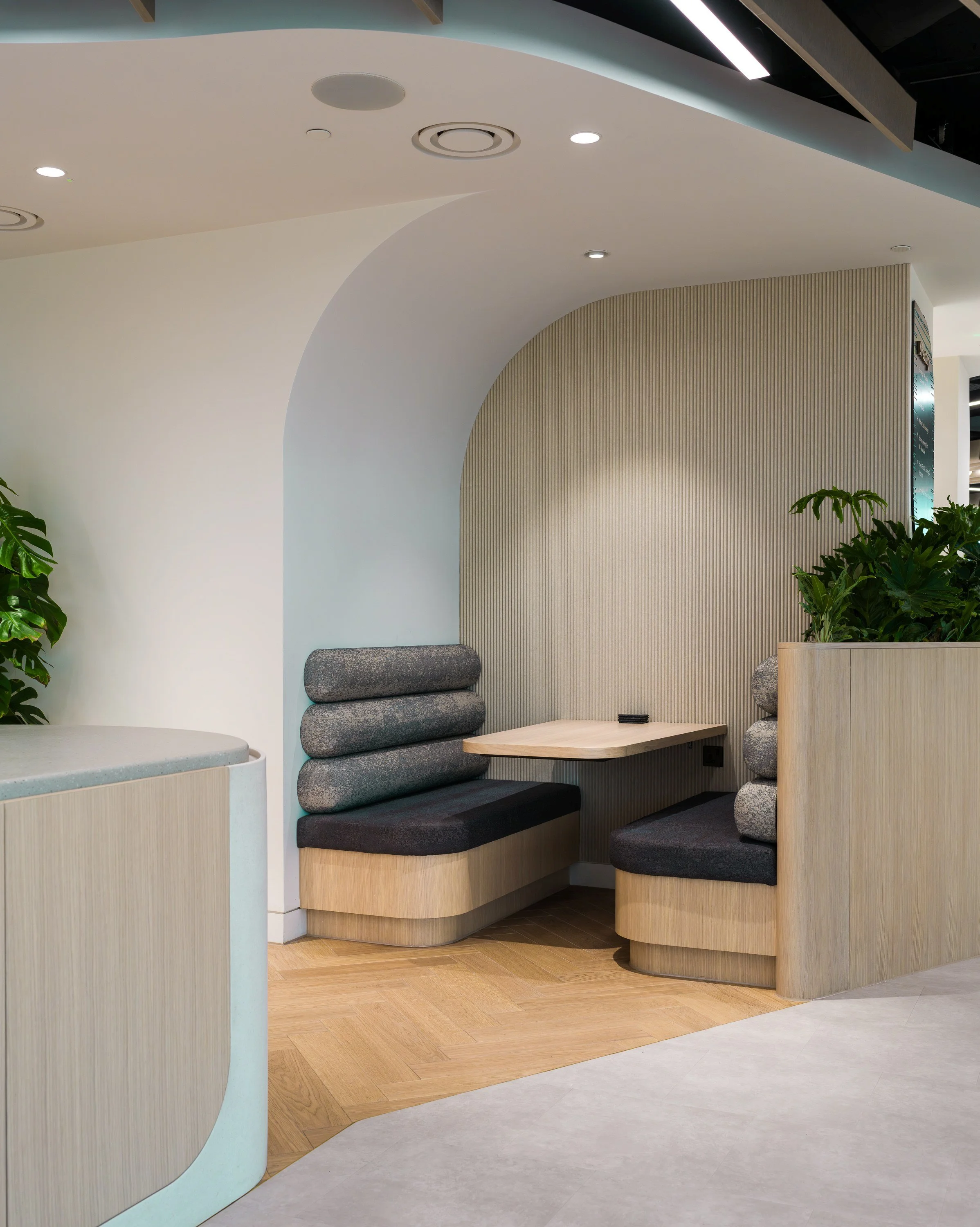 Modern seating area with wood paneling, built-in bench with dark cushioned seats, and green plants.