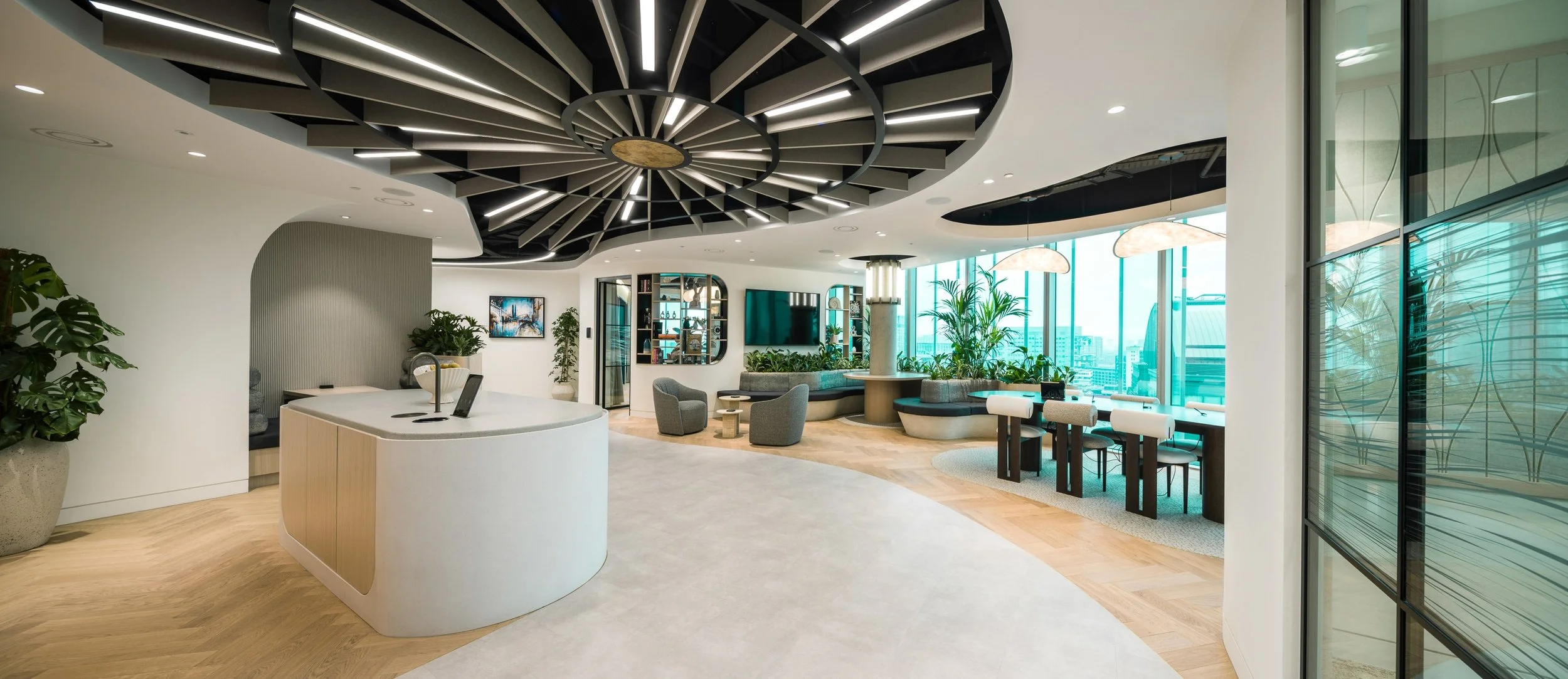 Curved reception desk and breakout workspace at Chancery Place, Manchester, with sculptural ceiling feature, biophilic planting and floor-to-ceiling glazing overlooking the city.