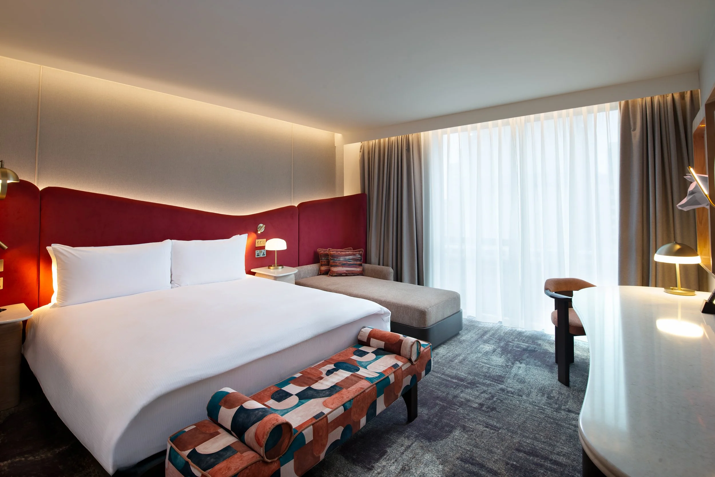 Guestroom at Hilton London Bankside featuring a sculptural red upholstered headboard, bespoke artwork, contemporary furnishings and interiors inspired by the creative character of the Bankside neighbourhood.