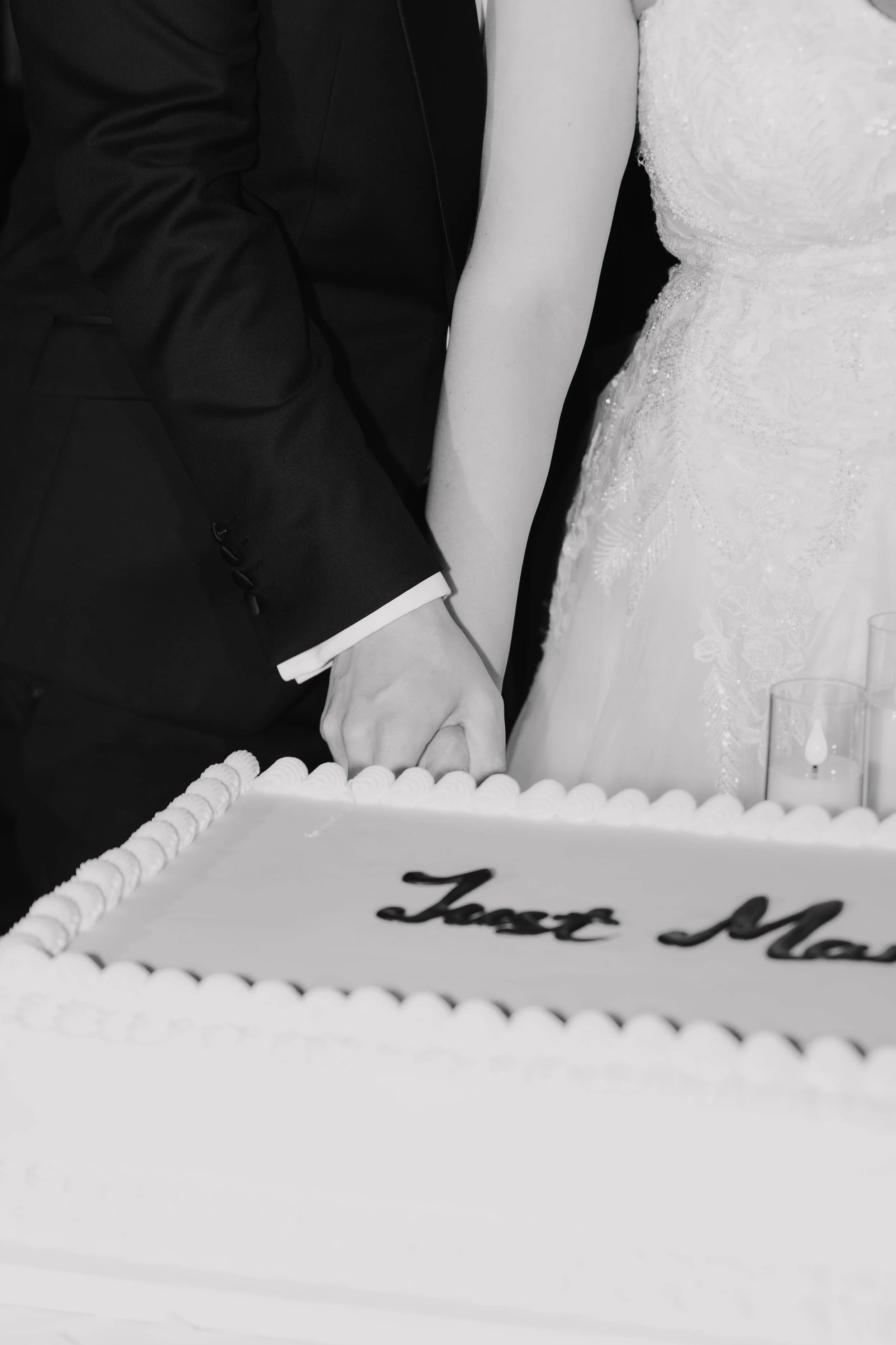 A bride and groom holding hands and cutting a wedding cake together at their wedding celebration.
