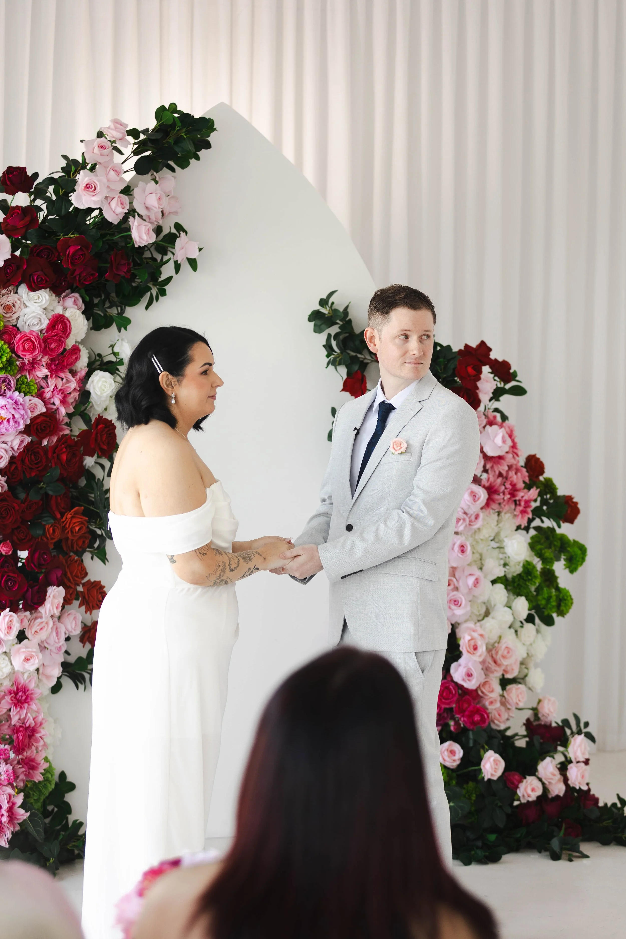 Shannon & Jarred's wedding at Faithwood Chapel – ceremony in front of a red, pink and white floral backdrop