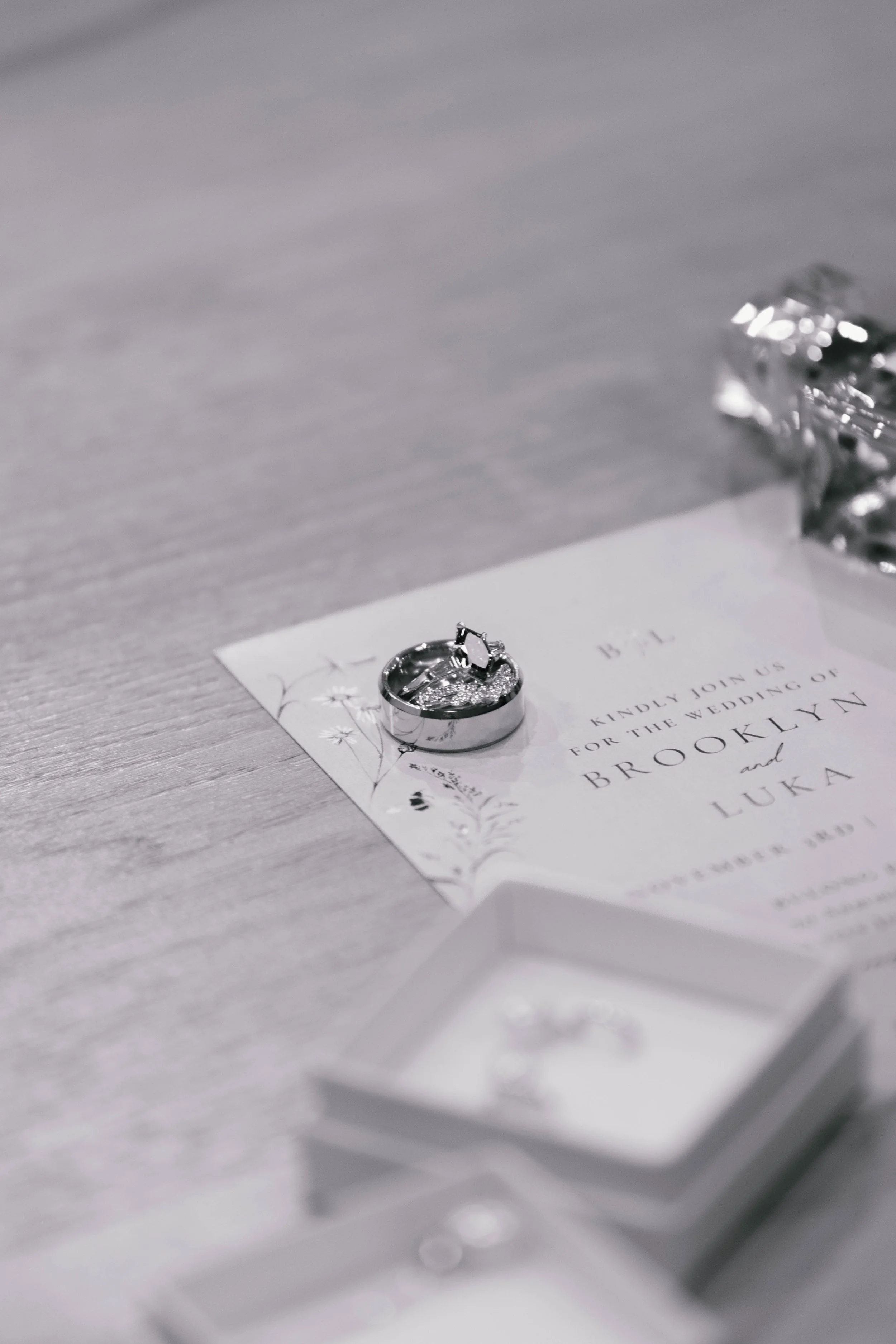 Wedding invitation card with rings placed on top, surrounded by jewelry boxes and silver foil, indicating a wedding celebration.