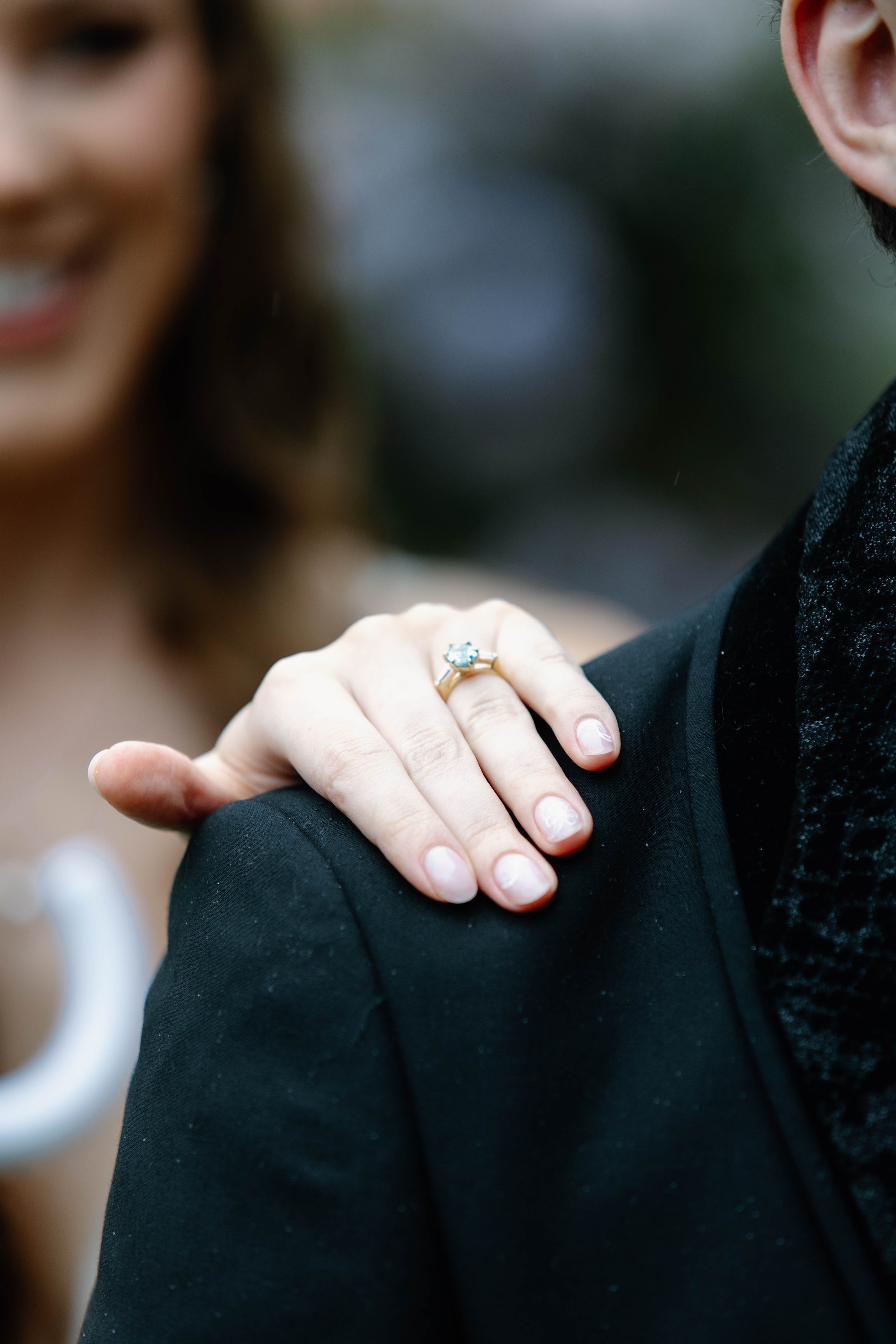 A woman with a wedding ring on her finger resting on a man's shoulder during a wedding or engagement moment.