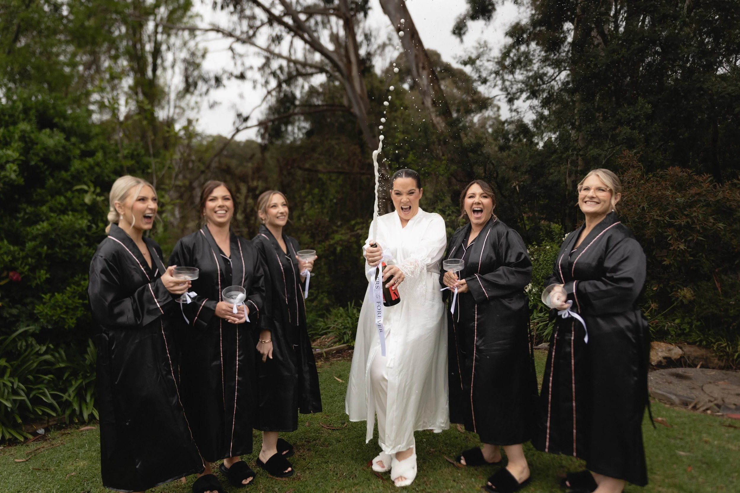 Court and her bridesmaids popping champagne in the garden before her wedding at The Stirling Hotel, Adelaide Hills
