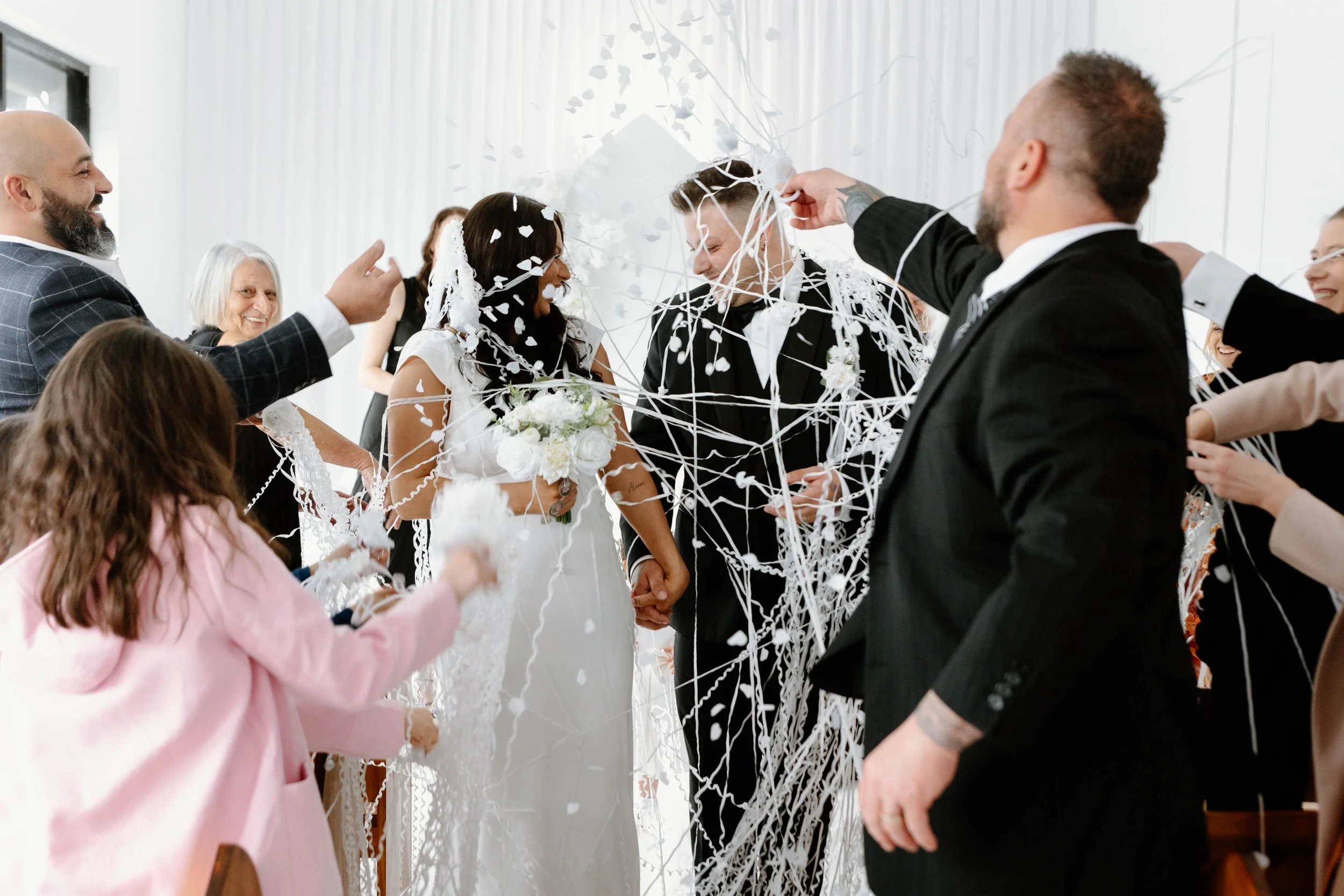 A wedding celebration with a bride and groom surrounded by friends and family throwing confetti and streamers.