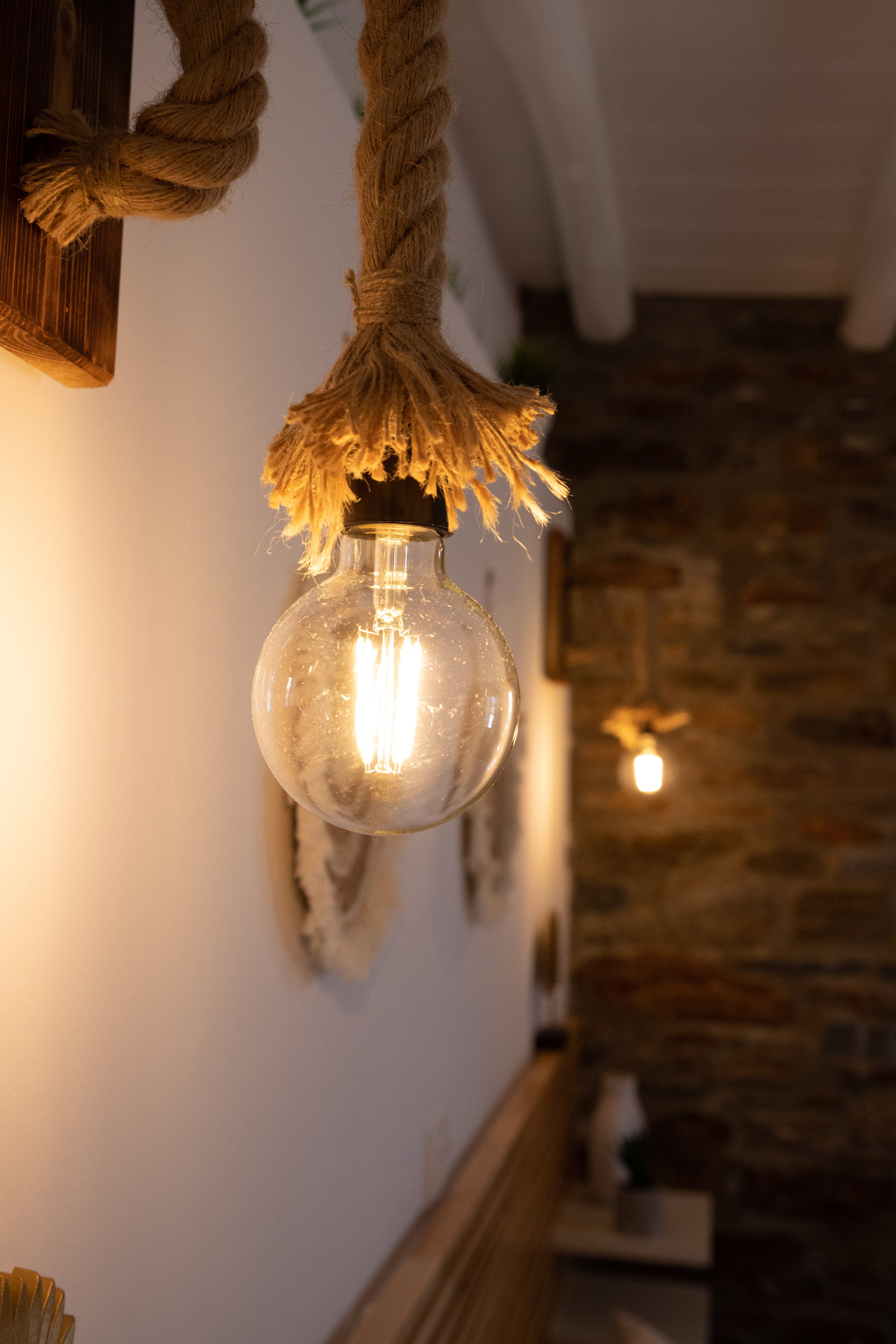 Close-up of a hanging light bulb with a rope covering the cord, glowing warmly, in a rustic interior setting.
