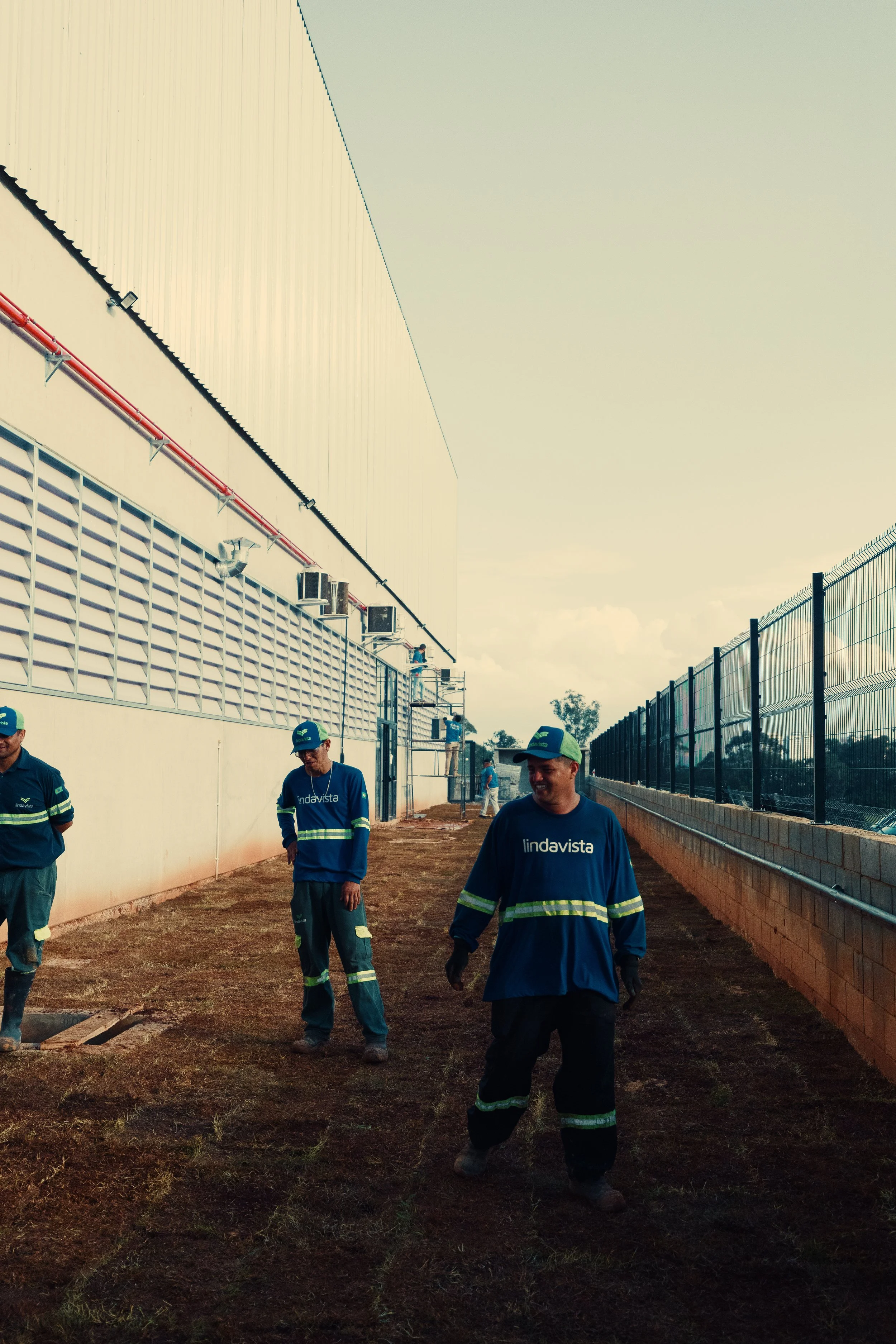 Pessoas vestindo uniformes de trabalho na construção de um muro de alambrado ao lado de uma parede de um prédio.