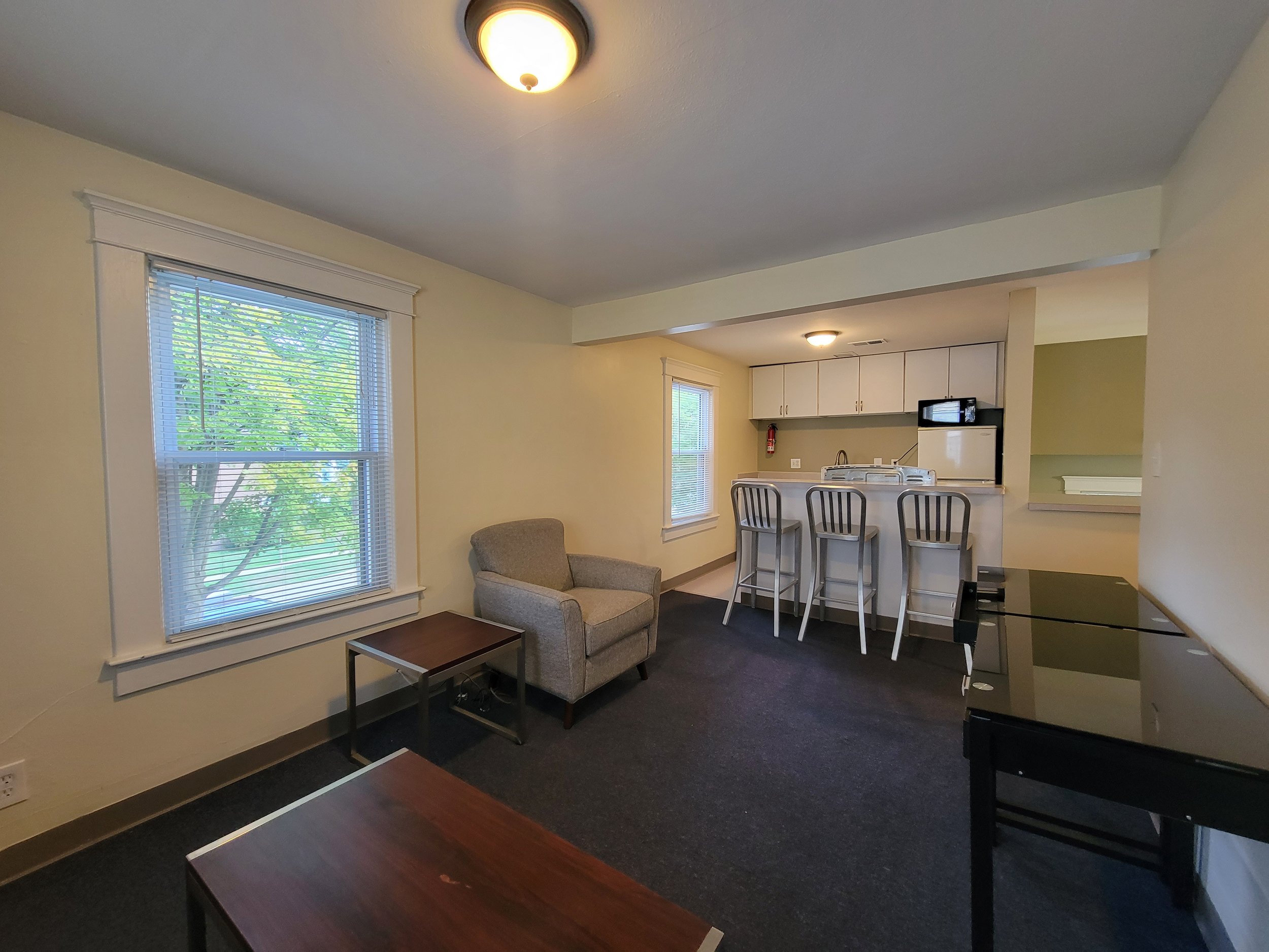 Interior of a small living space with a gray armchair, side tables, and countertop with barstools in rental property.