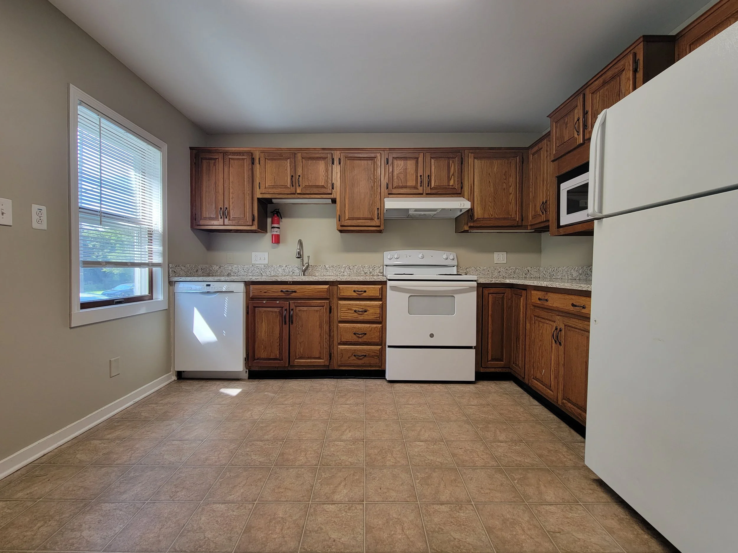 New rental property has kitchen with wooden cabinets, white appliances including a refrigerator, stove, dishwasher, and microwave, beige walls, and tiled floor.