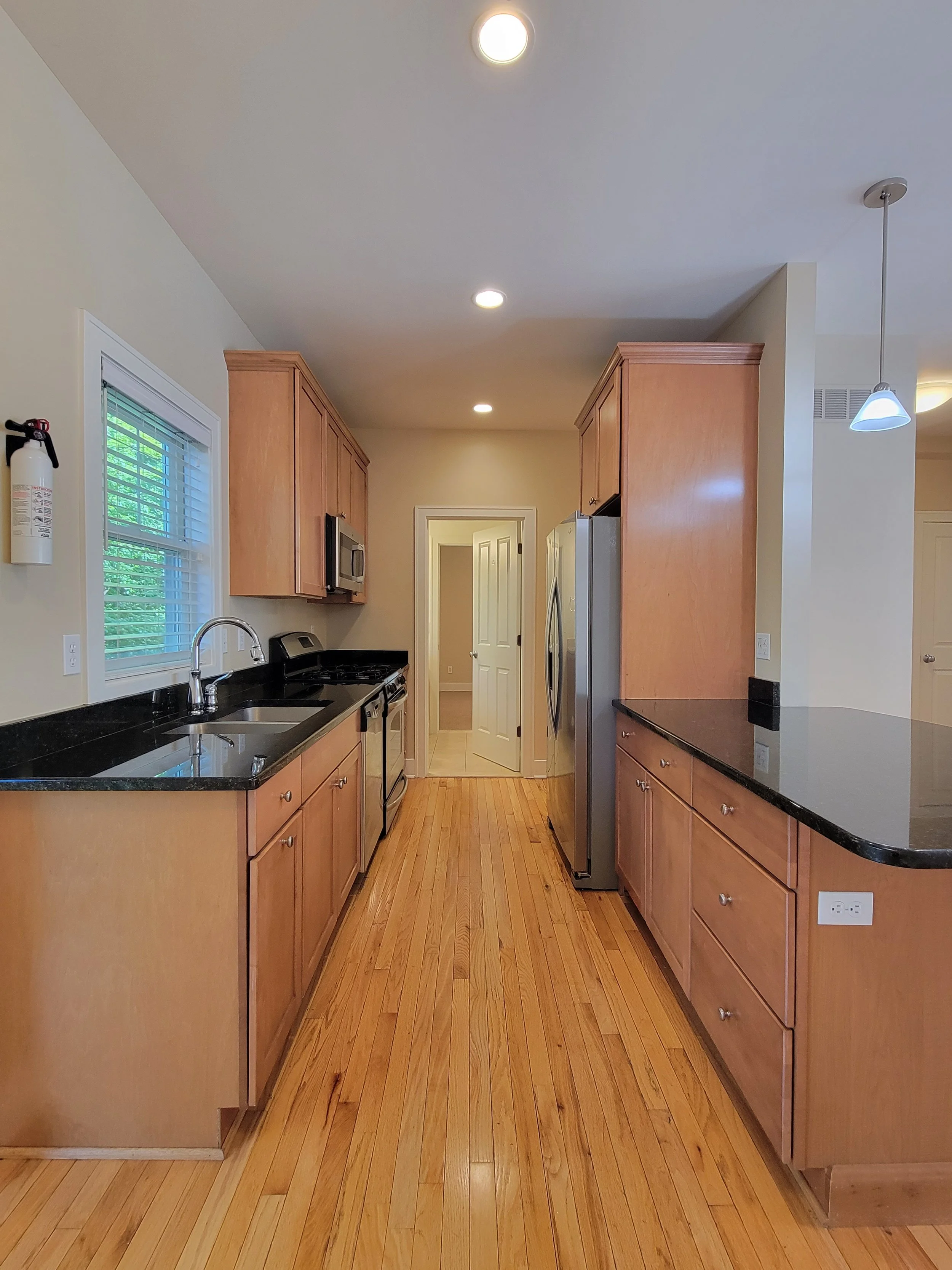 An Ann Arbor housing company's modern kitchen with wooden cabinets, black countertops, stainless steel appliances, and hardwood flooring.