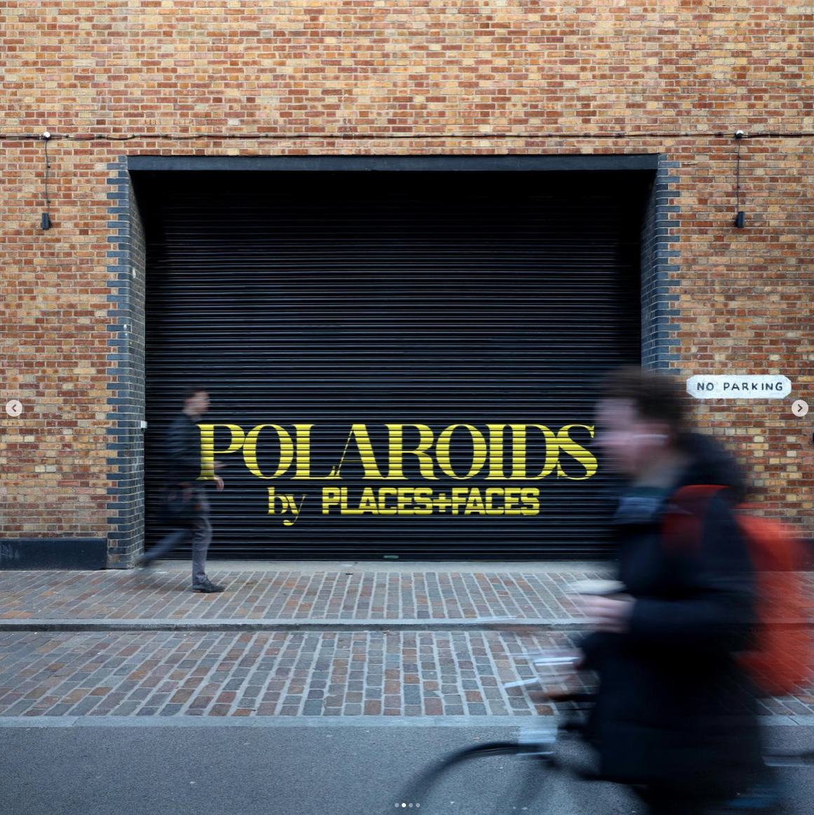 A black roller shutter door with yellow text that reads 'POLAROID by PLACES+FACES' on a brick building. A small white sign on the right says 'NO PARKING'. Two blurred people are walking past, one on each side of the image.