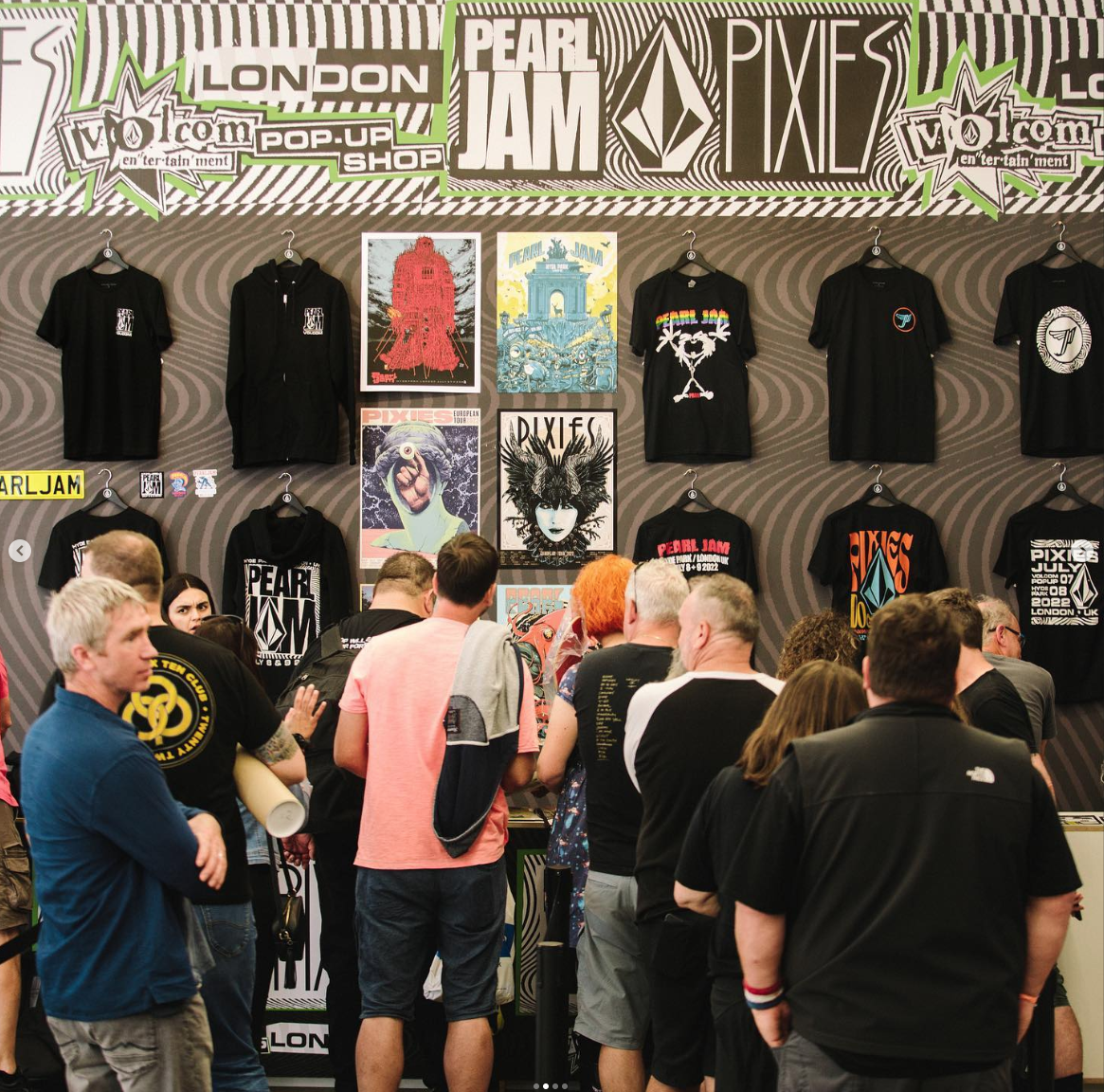 People gathered at a Pearl Jam pop-up shop in London, browsing band T-shirts and posters displayed on the wall.