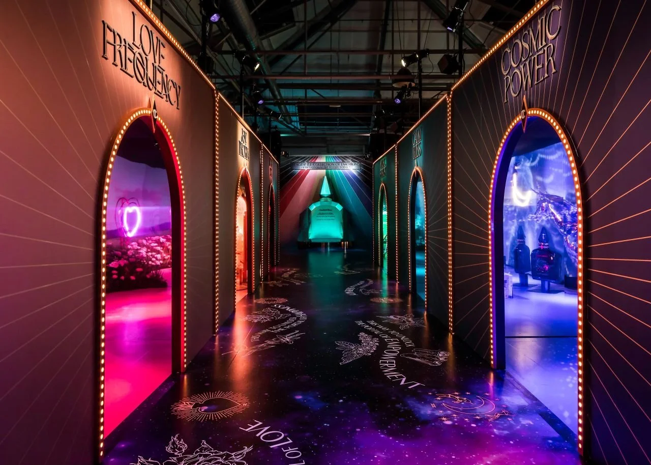 Colorful hallway with neon lights, themed around love, love frequency, and cosmic power, leading to illuminated room displays with space and nature motifs.
