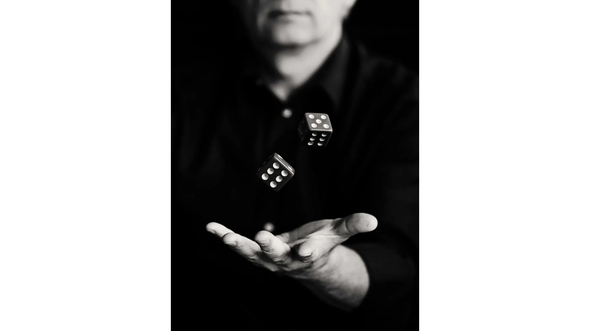 Black and white image of a person tossing two dice in the air with one hand