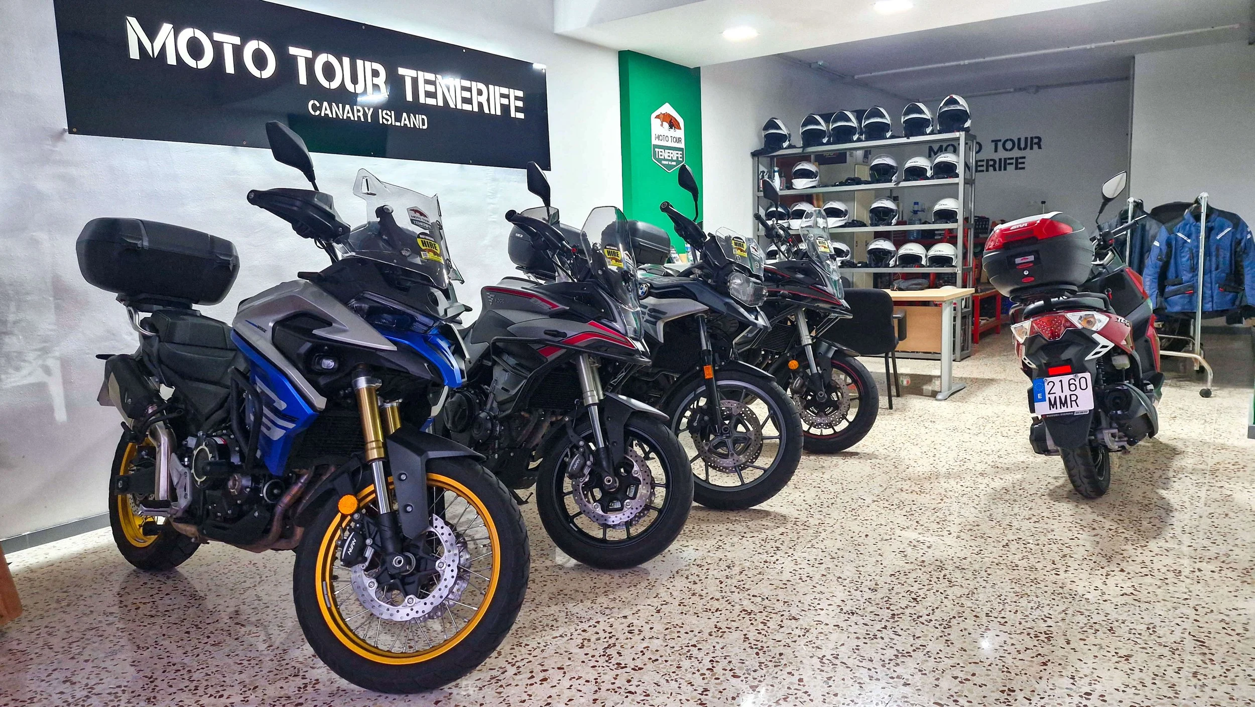 Mostrador con varias motocicletas en exhibición, cascos de motocicleta en estantes y accesorios de motociclista en tienda de alquiler en Tenerife, Canary Island.